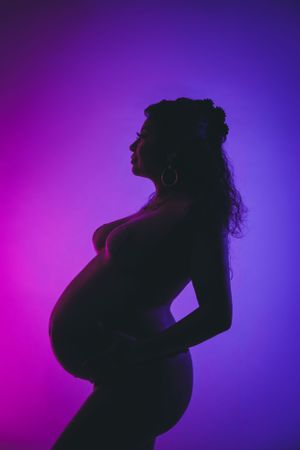 Silhouette of a pregnant woman in profile against a vibrant purple background. maternity photoshoot