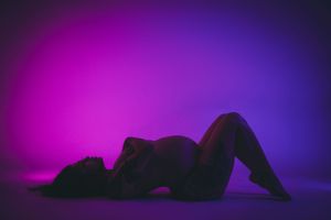 Silhouette figure lying down against vibrant purple and blue gradient background in artistic lighting. maternity photoshoot