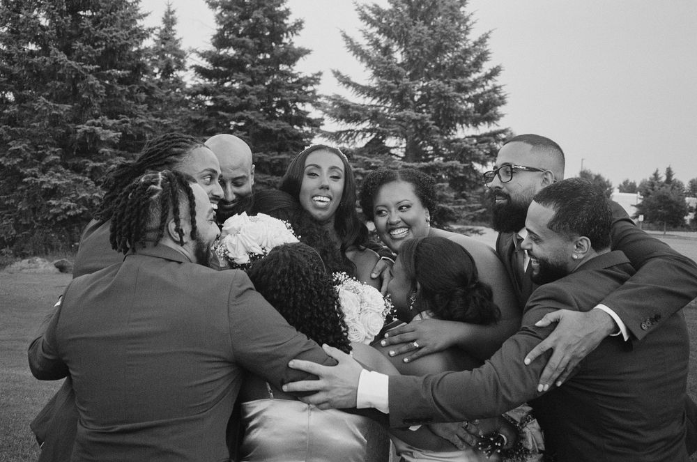 Wedding party shares a joyful group hug outdoors in black and white photo.