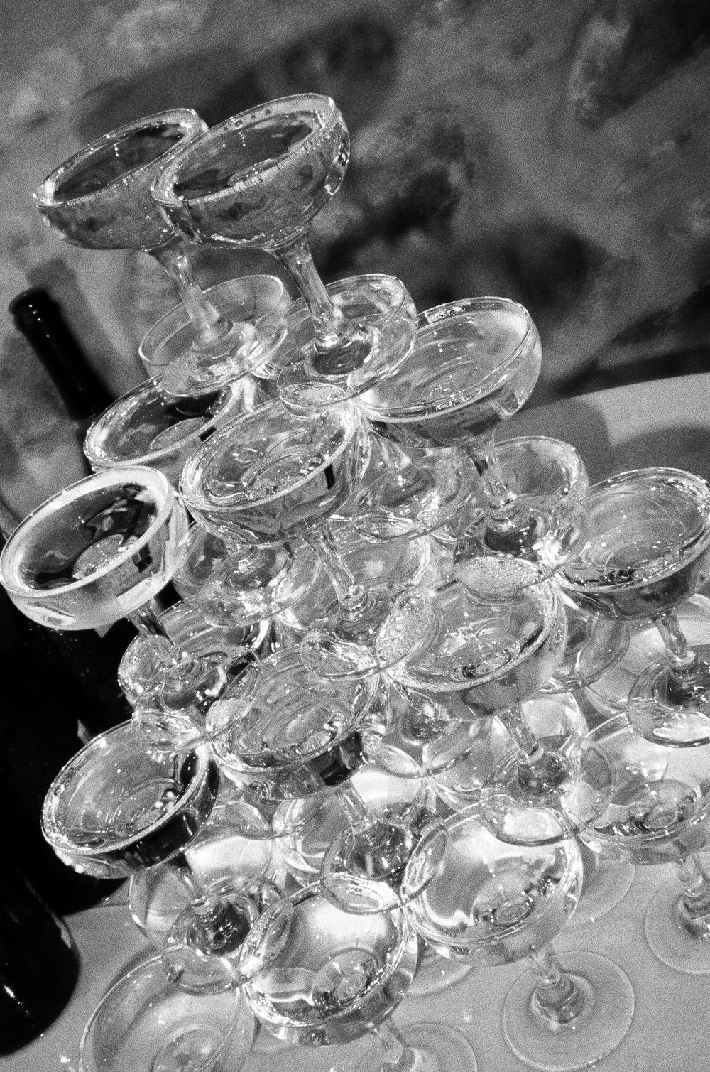 Black and white photo of an elegant champagne tower with stacked coupe glasses at a formal celebration event.