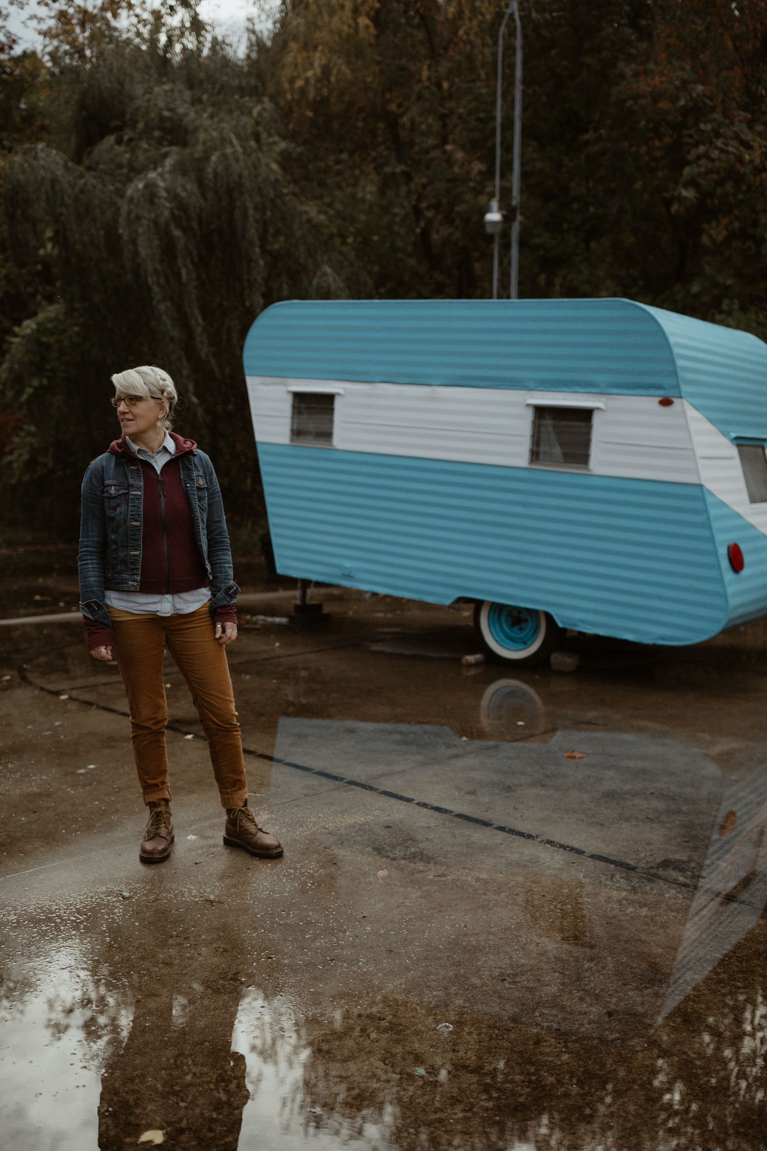 A vintage blue and white camper trailer sits parked on wet ground during an overcast day.