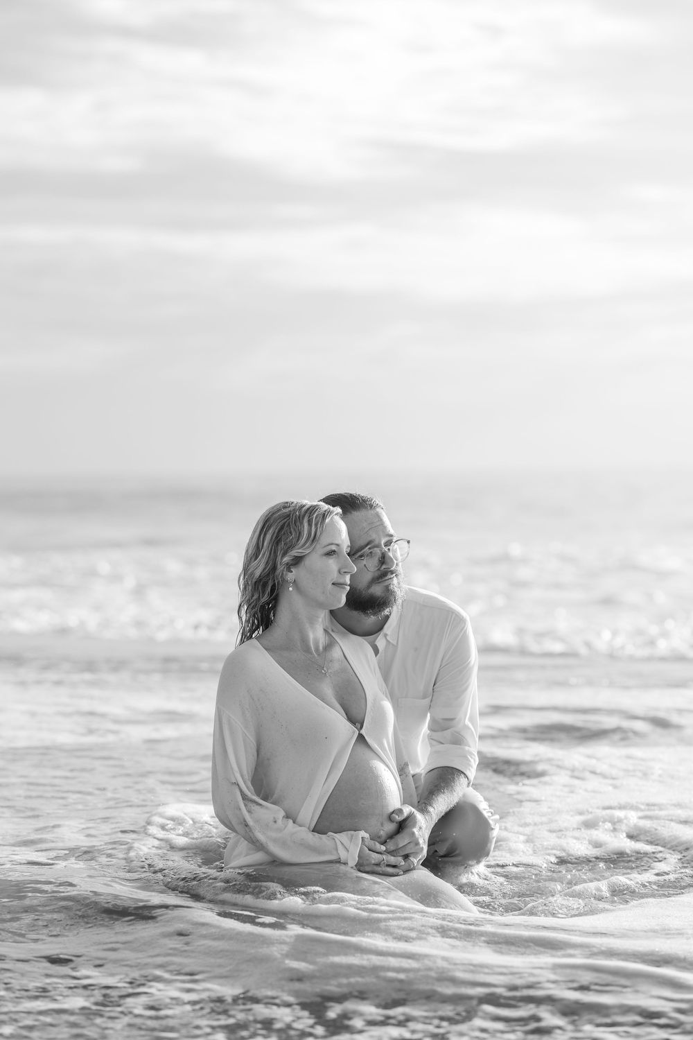 A romantic black and white photo series of a couple playfully embracing in ocean waves.