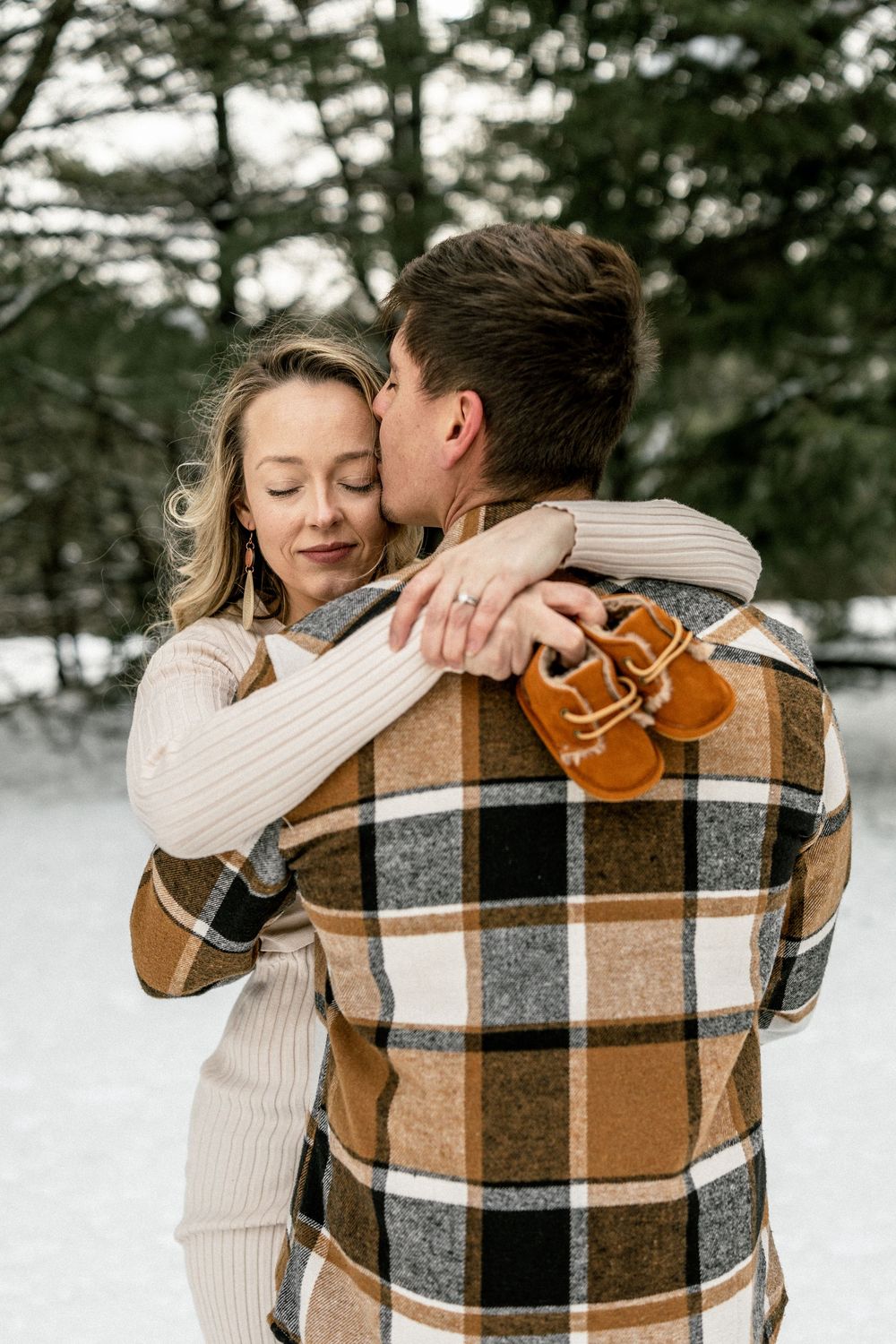 Couple in cozy winter sweaters embrace outdoors in the snow, wearing cream and plaid patterns.