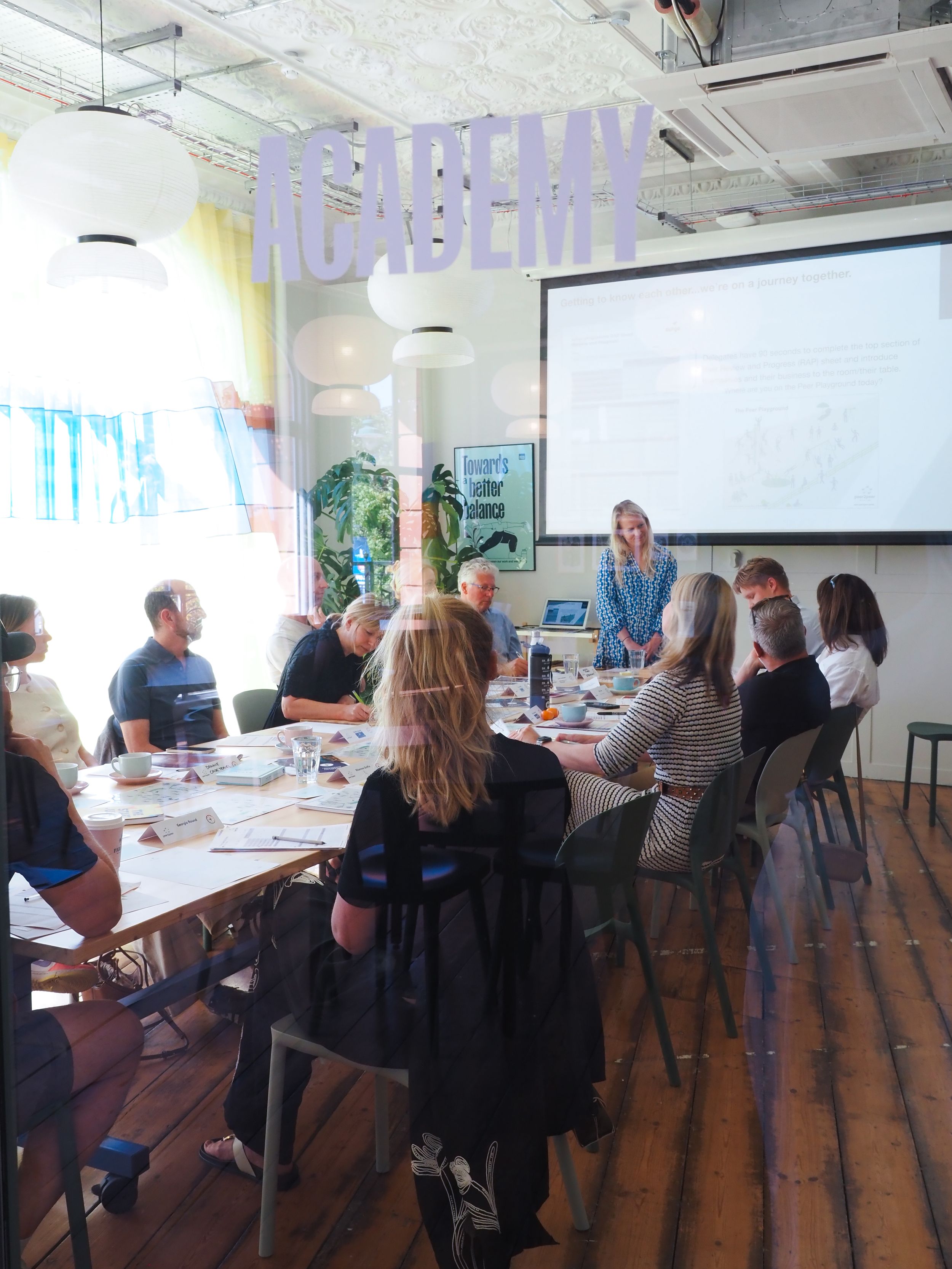 A group of professionals seated around tables during a workshop session in a modern office space with purple decor elements.