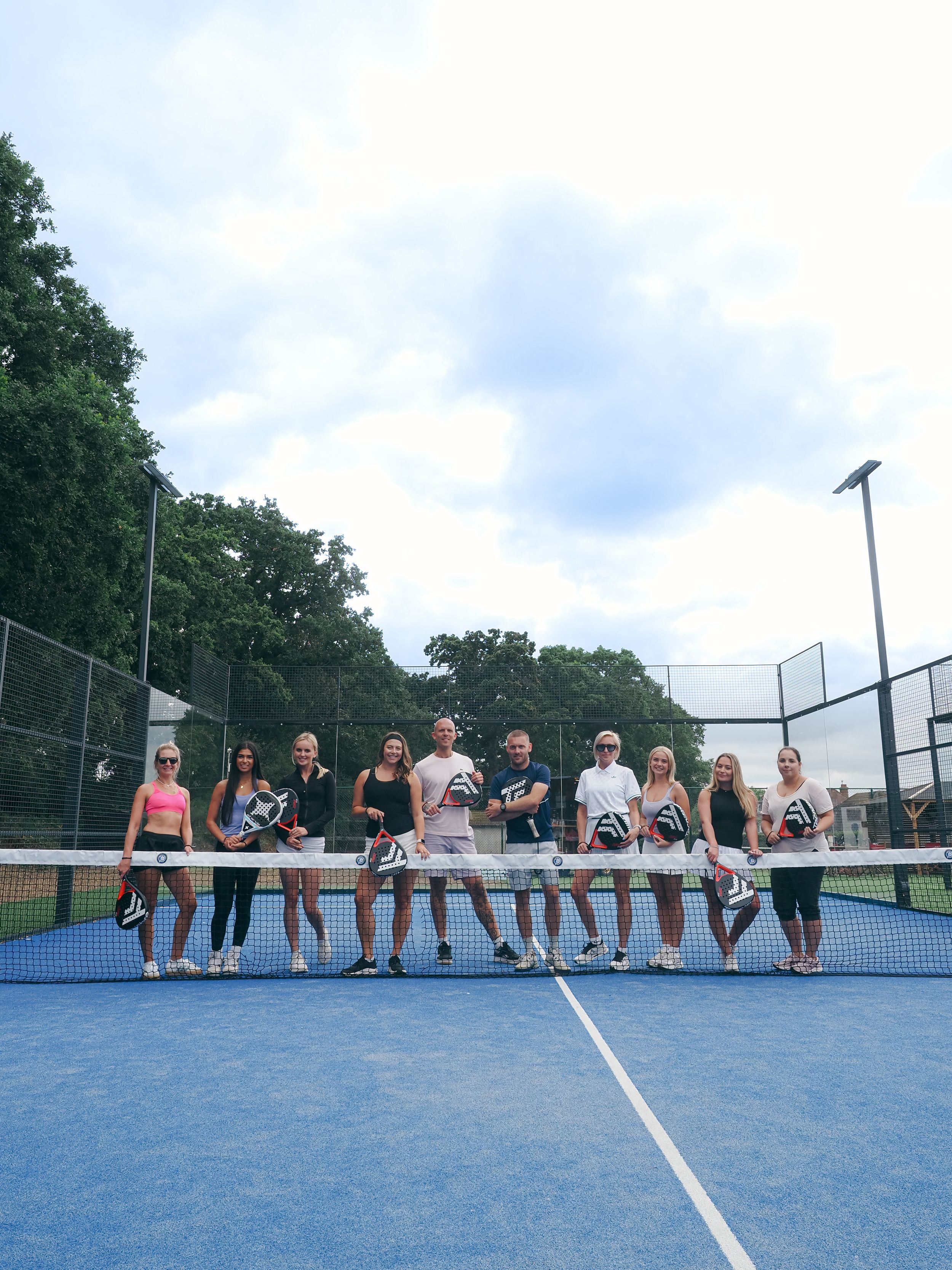 A group of people sitting in a row on a blue tennis court looking out towards the playing area.