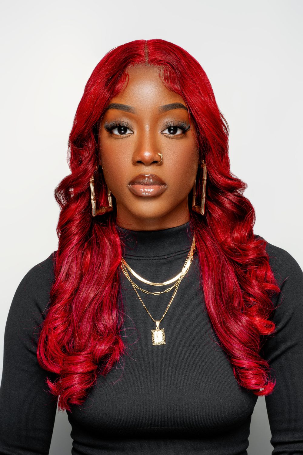 Studio portrait showcasing flowing red hair, elegant makeup and layered gold necklaces.