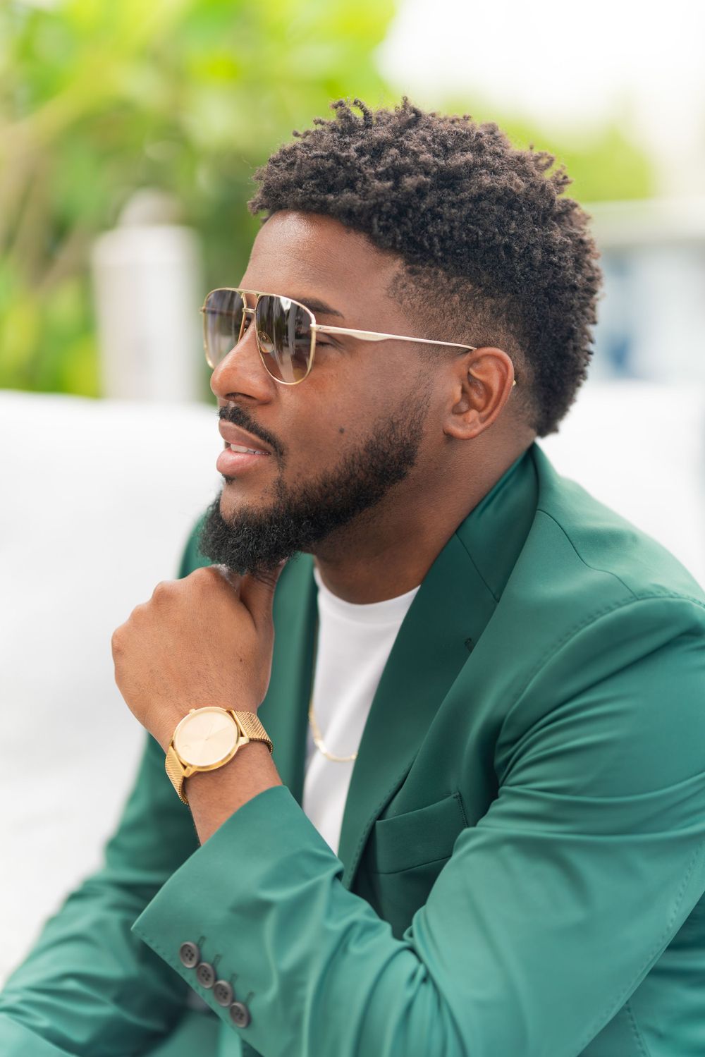 Stylish portrait of man in green blazer wearing sunglasses and gold watch.