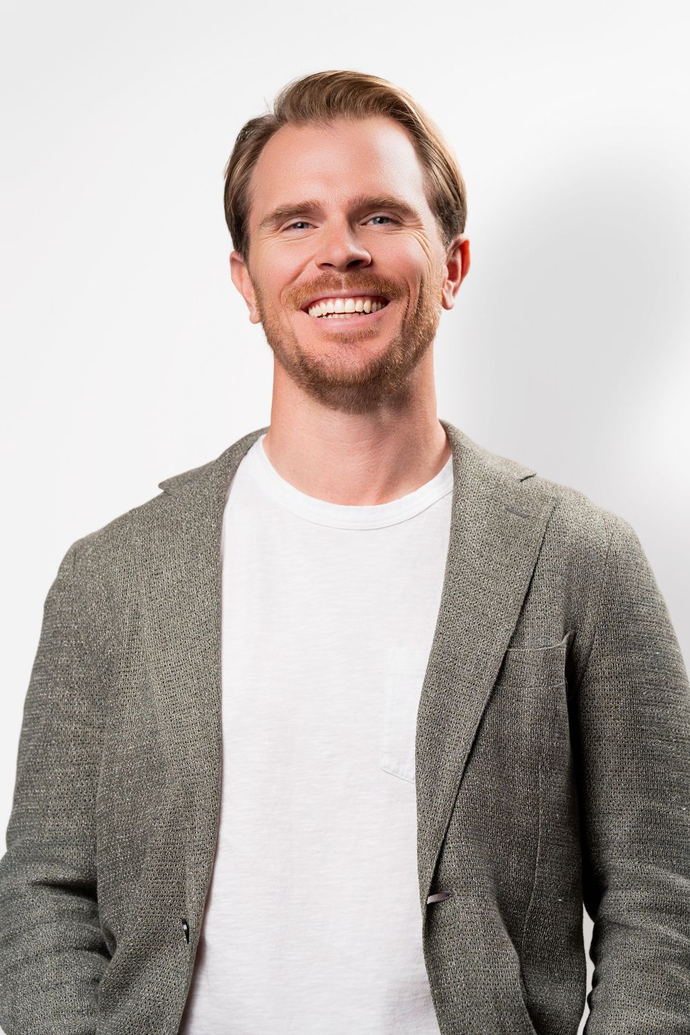 Professional portrait of someone wearing a gray blazer and white t-shirt against a light background.