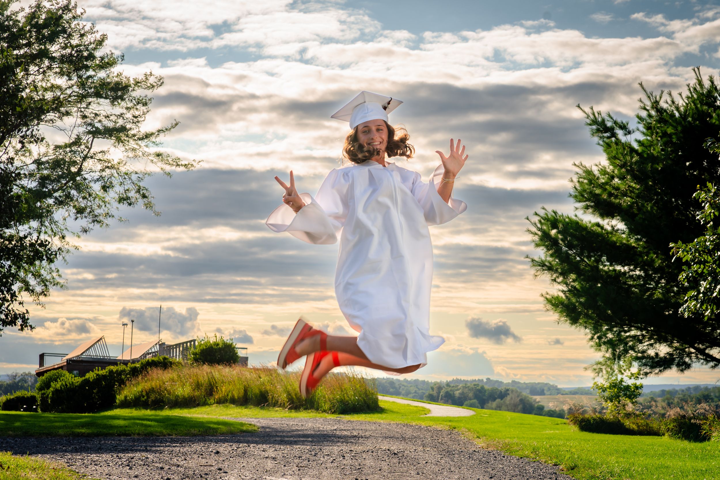 Joyful person in white dress jumping in the air against a dramatic sunset sky.