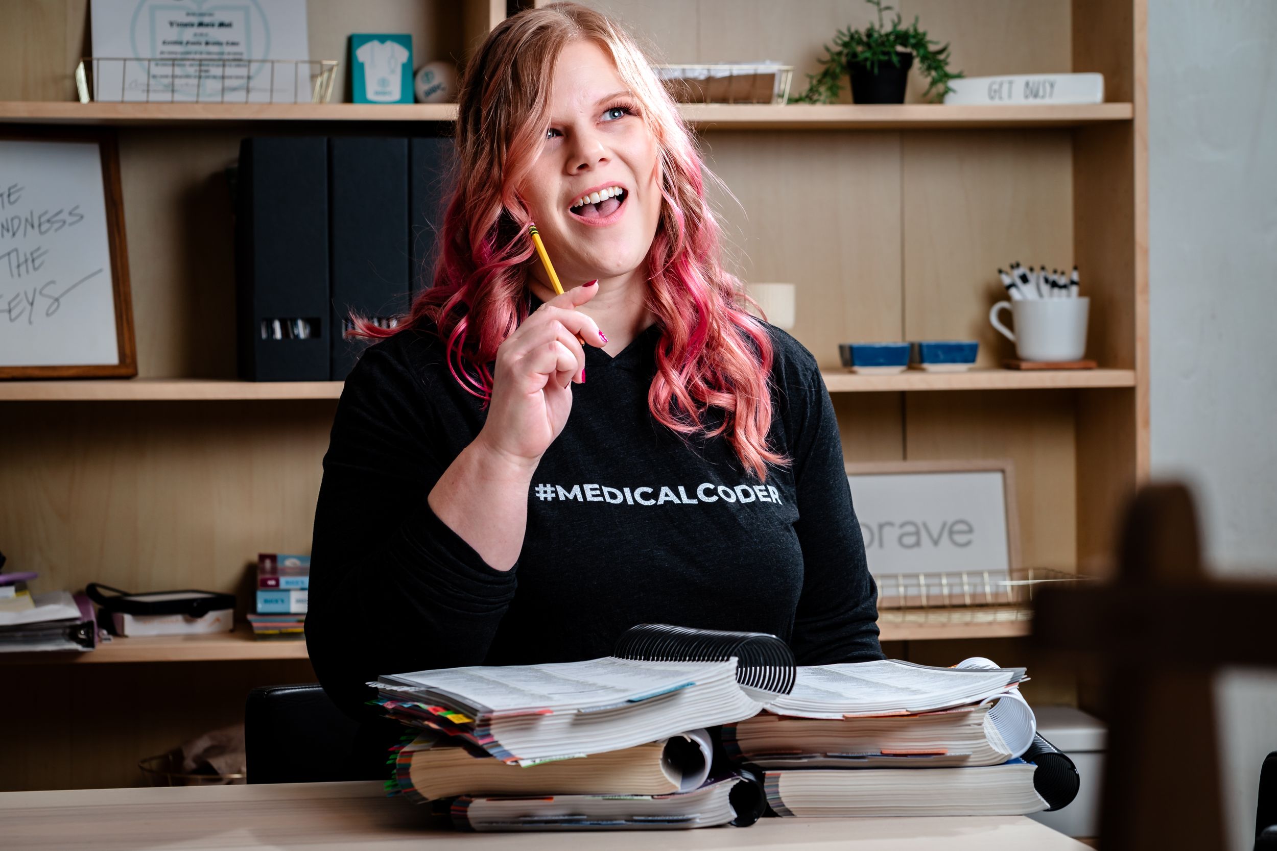 Professional working at desk with pink hair and laptop in modern office setting.