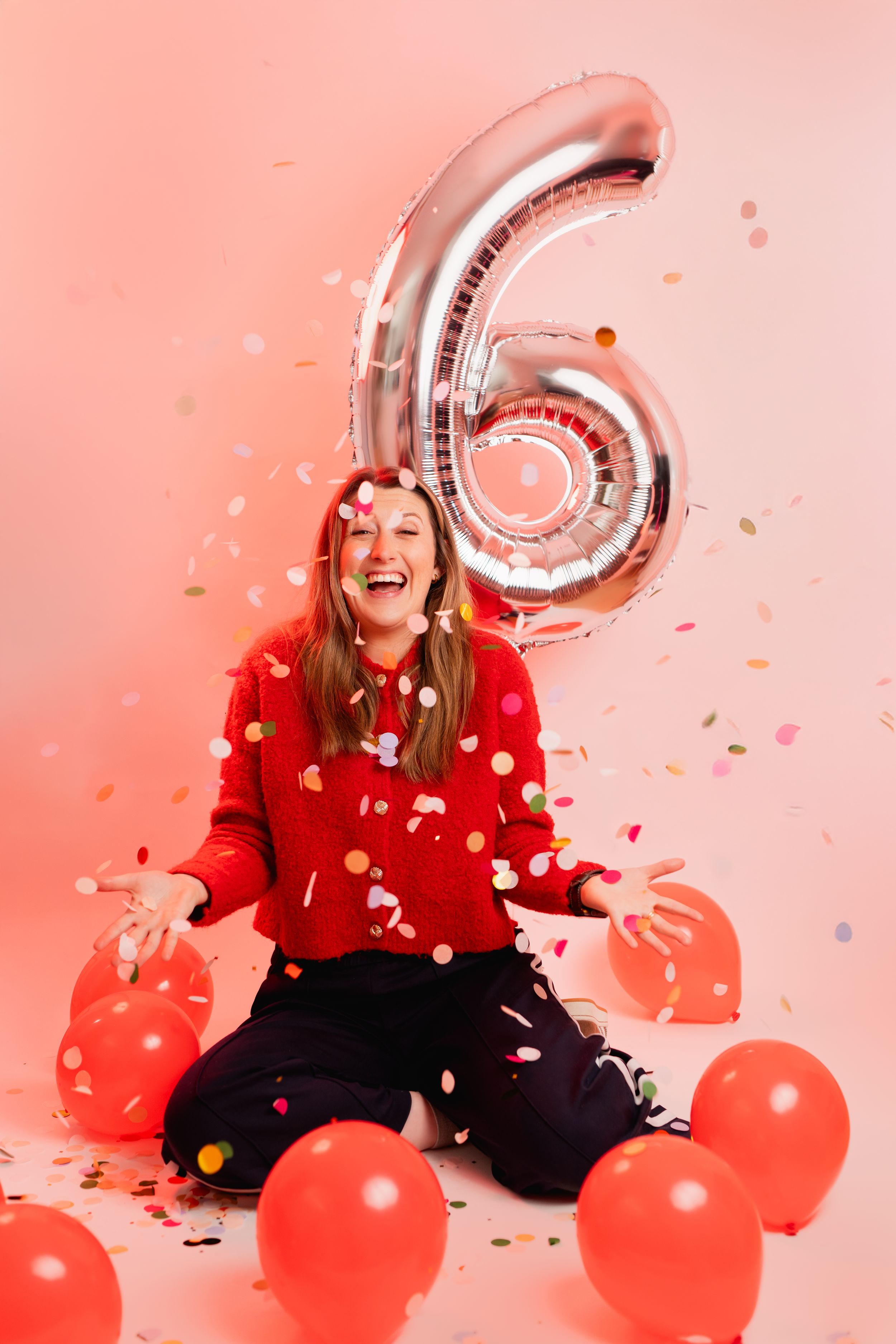 A person in a red sweater celebrates with balloons and confetti against a pink background in a festive photo series.
