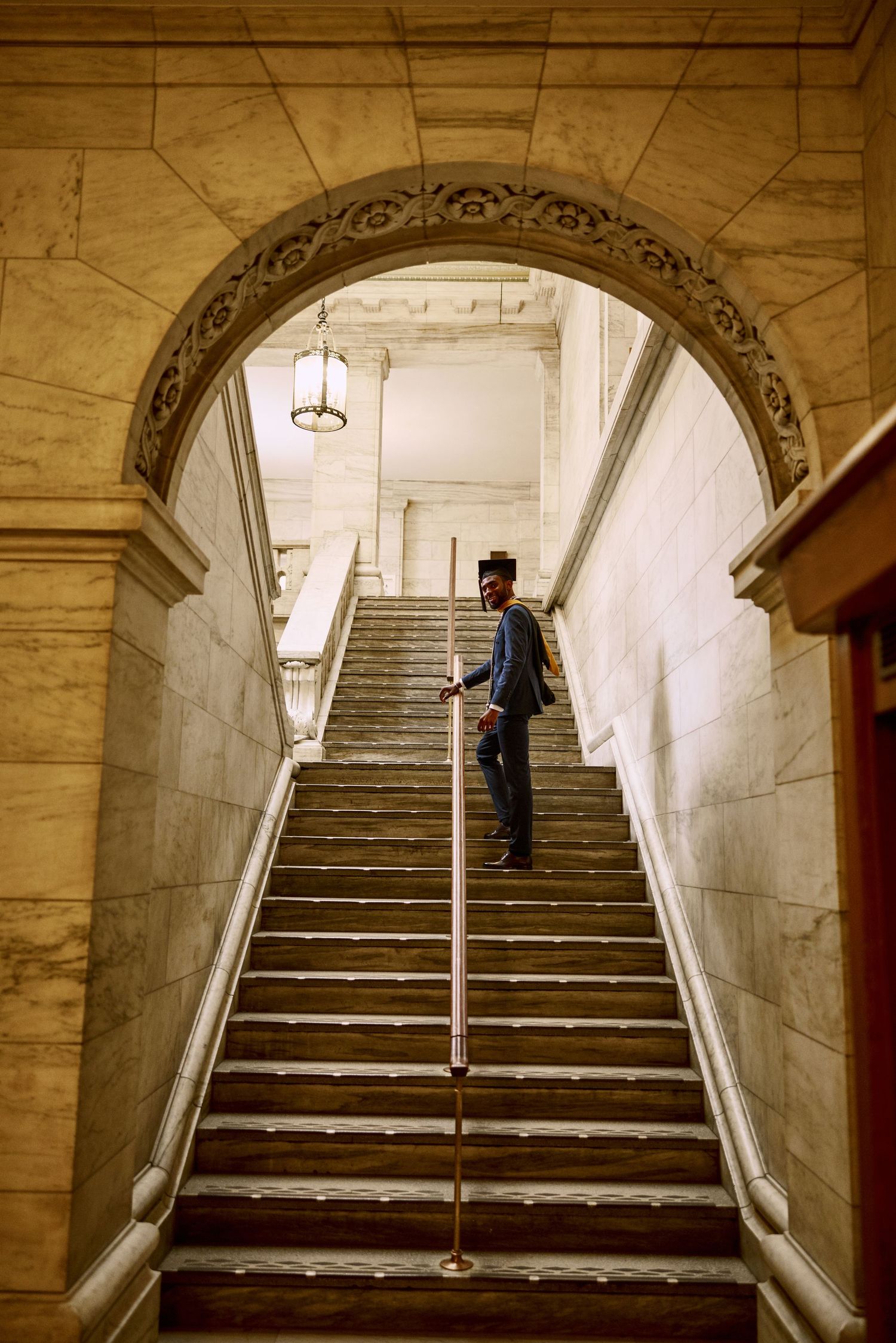 Person ascending ornate marble staircase with decorative archway in historic building interior.