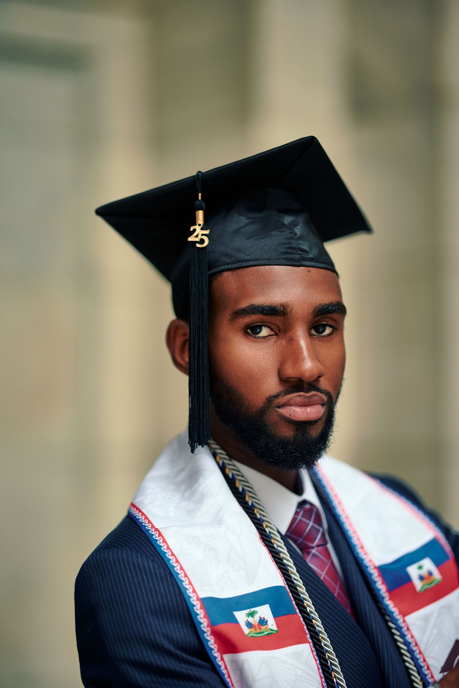 Graduate wearing a navy suit and graduation cap with Haitian flag stole during commencement ceremony.