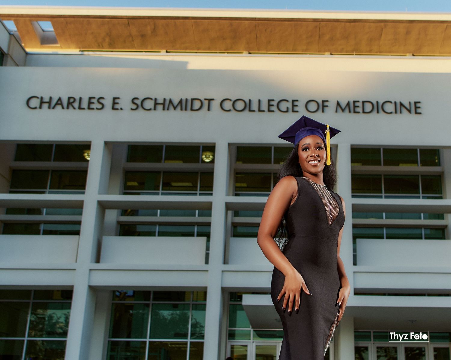 Graduation portrait of a student in front of a university building, dressed in a sleek outfit, celebrating a milestone achievement.