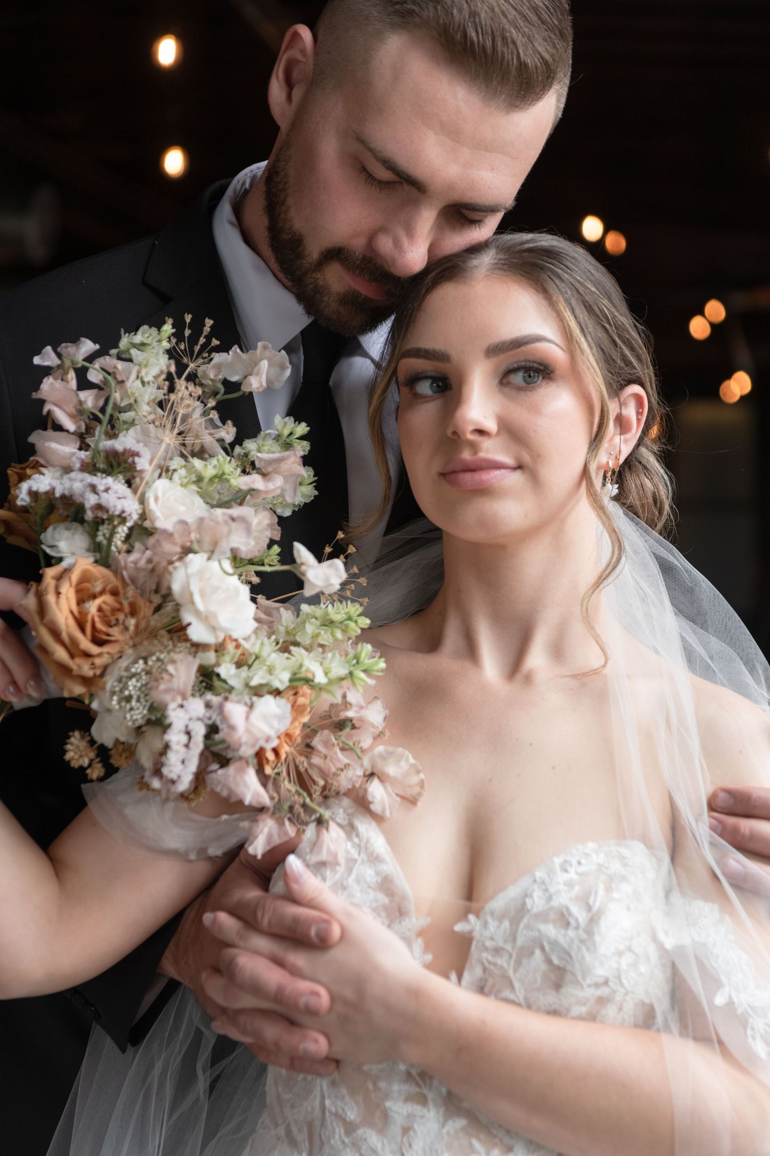 Romantic wedding portrait with couple holding elegant pastel floral bouquet.