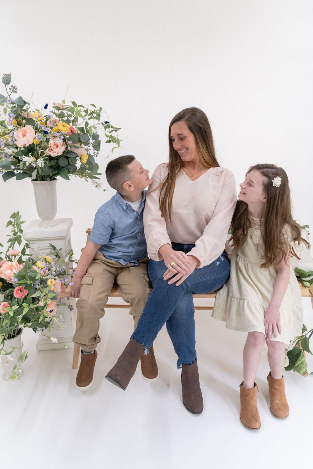 Casual family portrait with floral decor showing a mother and two children sitting together on a white bench.