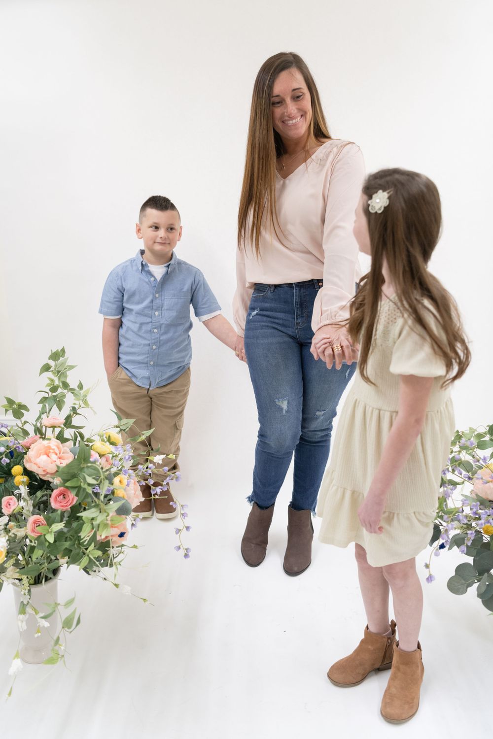 Three people stand among floral arrangements in a bright white studio setting.