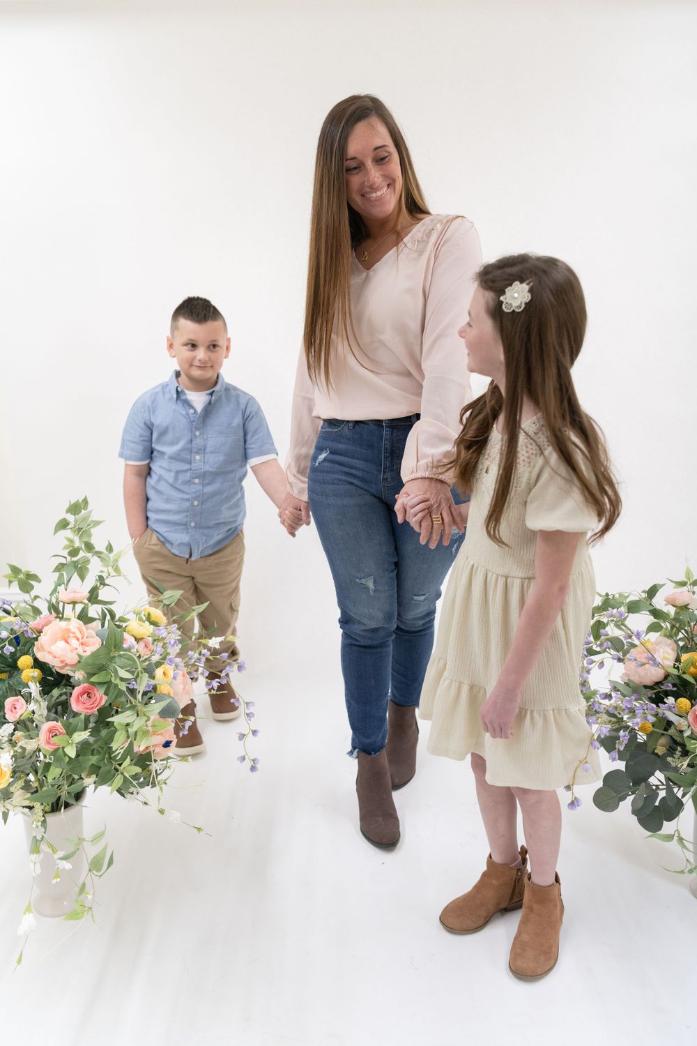 Candid family portrait with mother and children holding hands between floral arrangements.