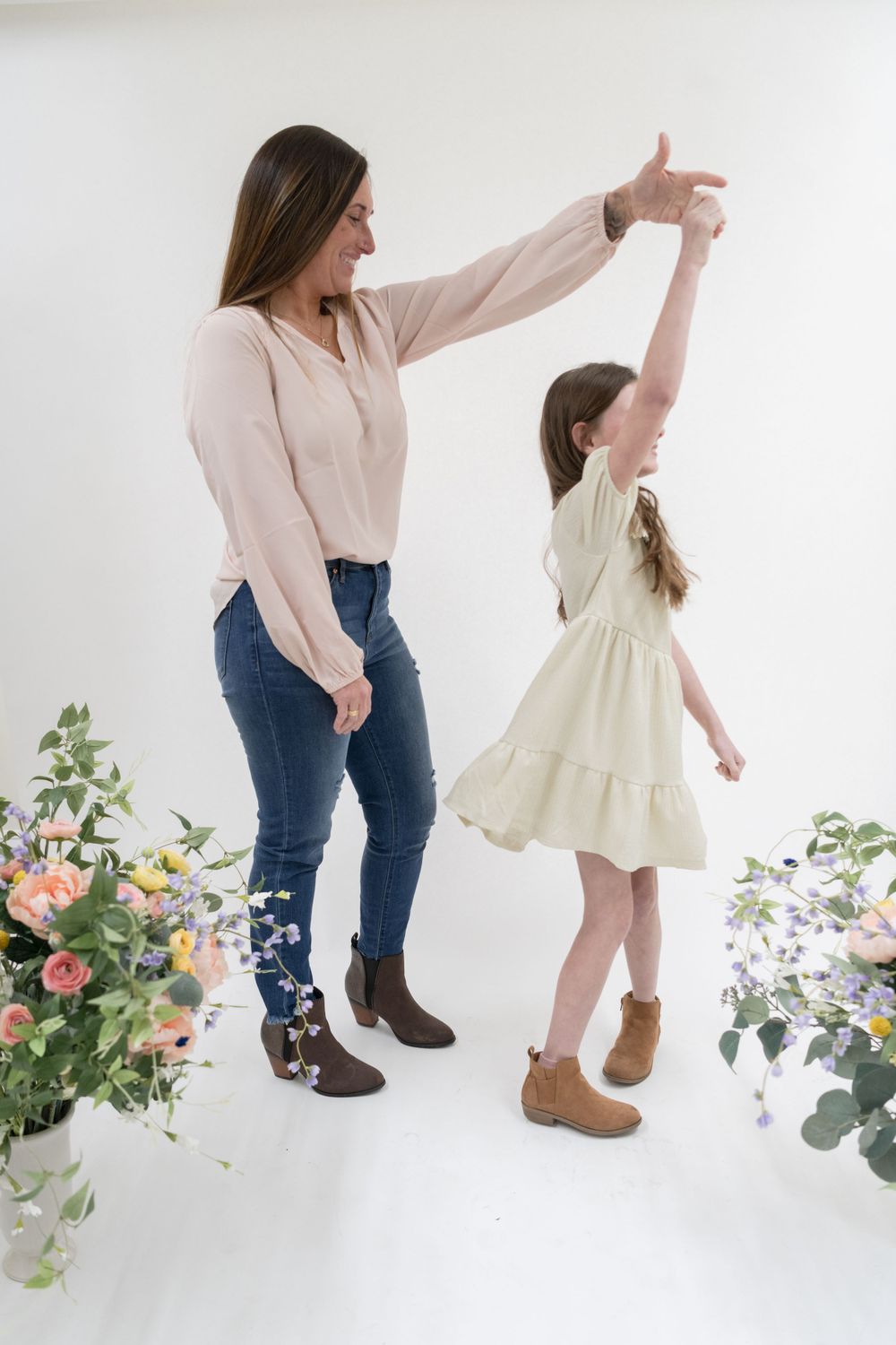 Two people dance and twirl among floral arrangements in a white studio setting.