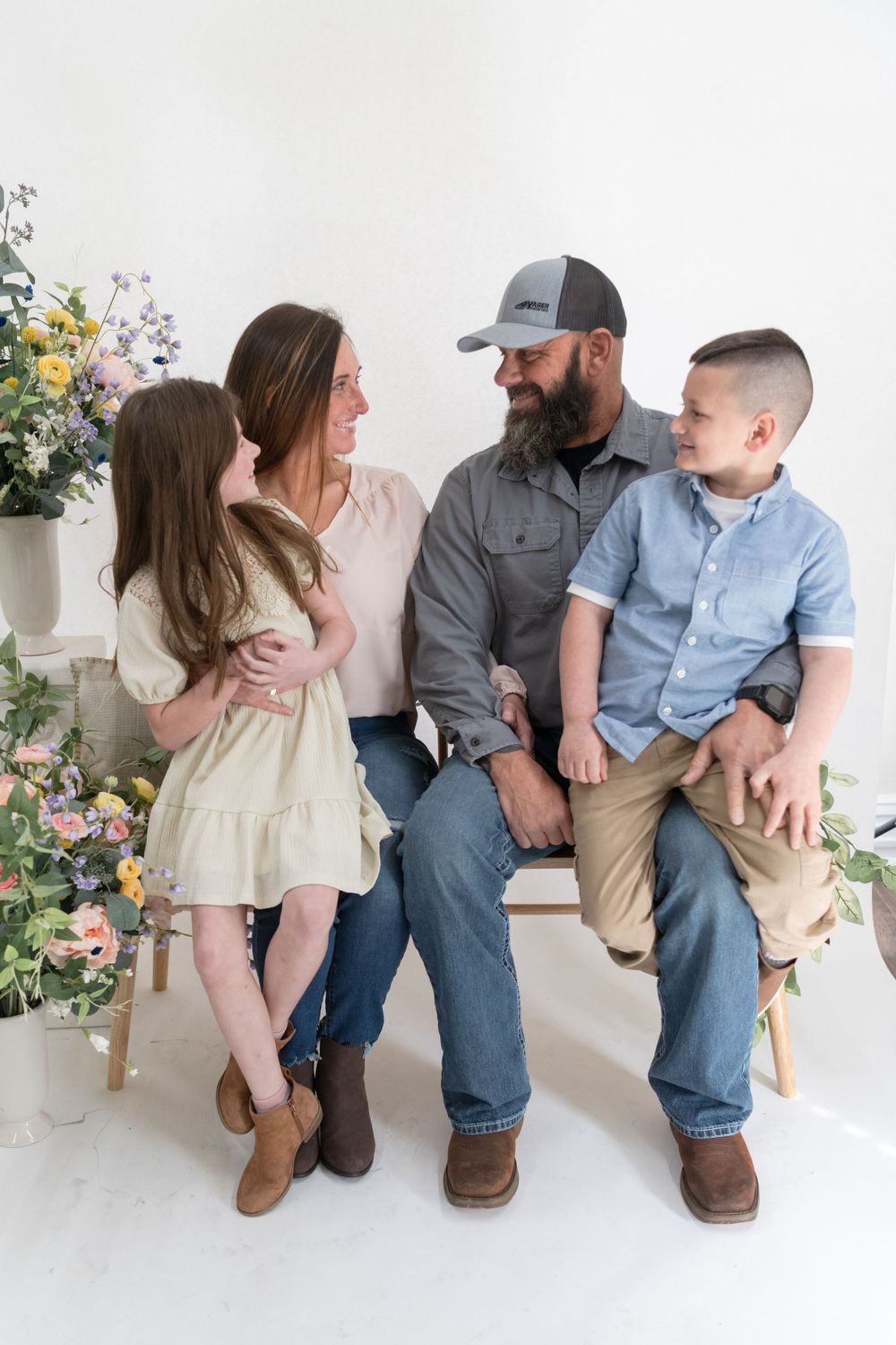 Family of four posing together on bench with colorful floral arrangements in studio setting.