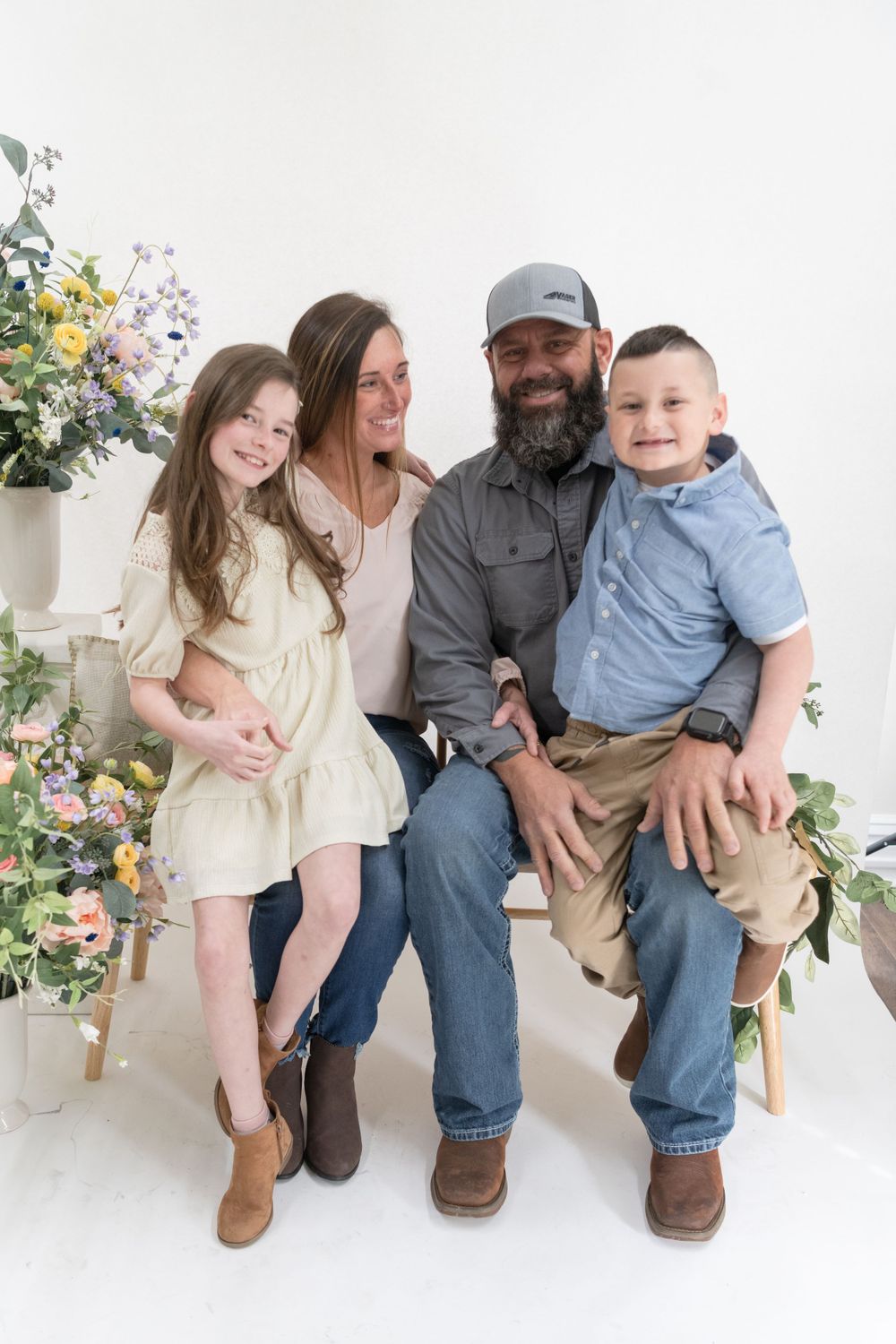 Family portrait with floral backdrop showing casual poses and warm smiles.