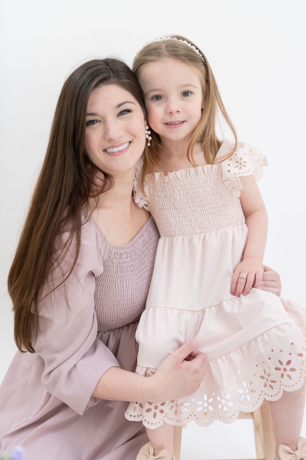 Portrait of family members in coordinating pink dresses sitting together against white background.