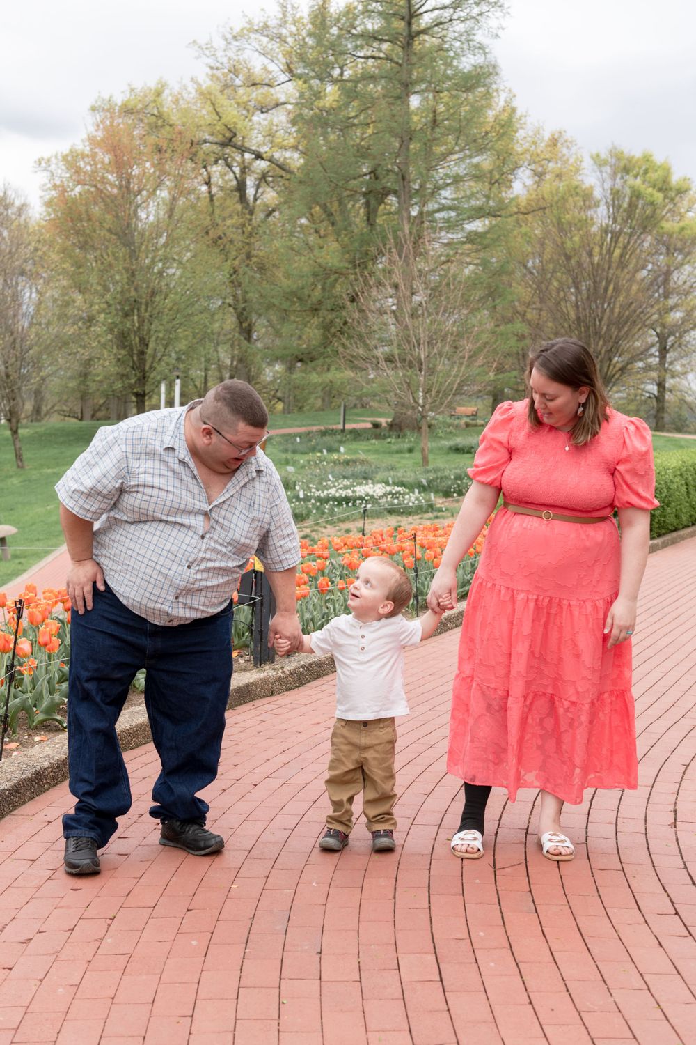 Family walking together on brick path surrounded by spring tulips and trees.