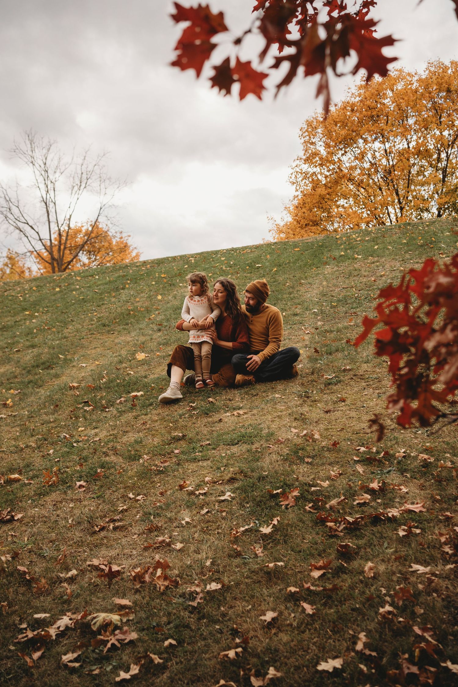 Autumn scene with people sitting on hillside among fallen red and orange leaves.