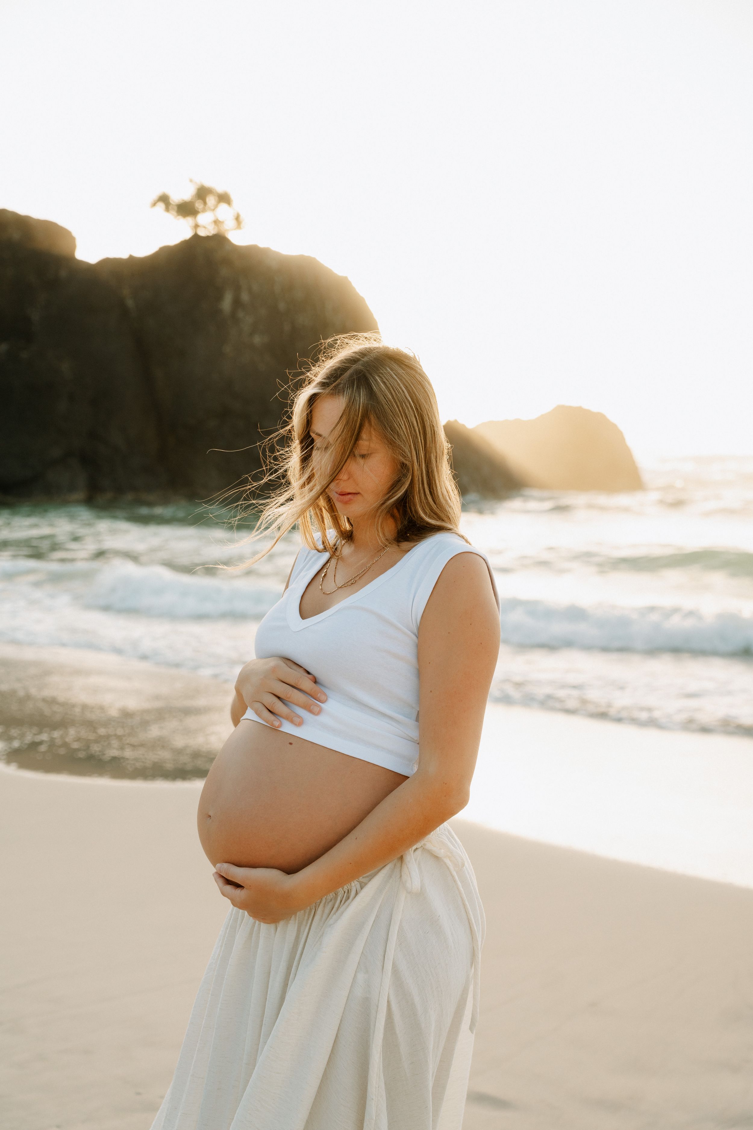 Maternity photo session on sandy beach at sunset with dramatic coastal cliffs.
