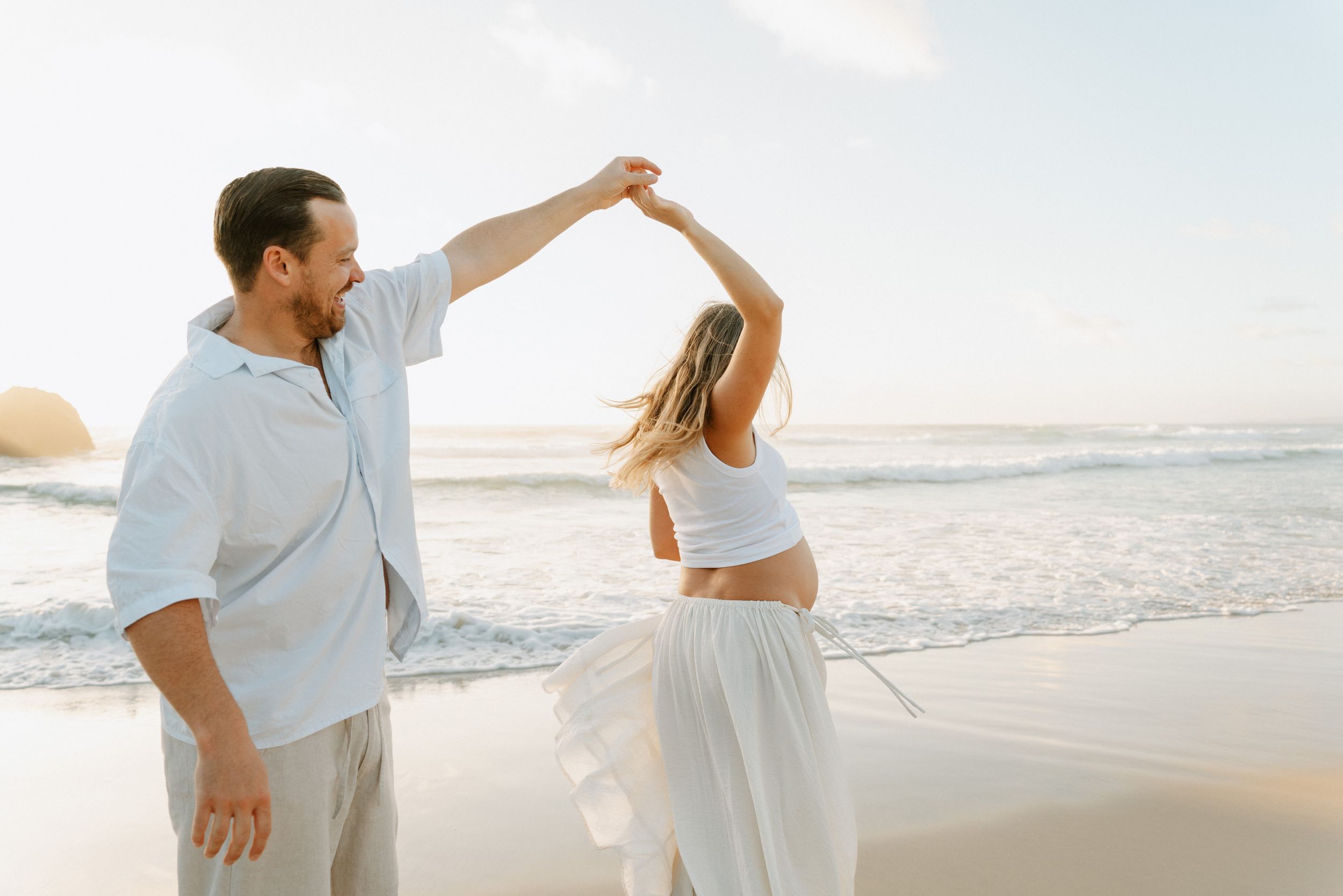 Joyful dancing and splashing in ocean waves during sunset beach photoshoot.