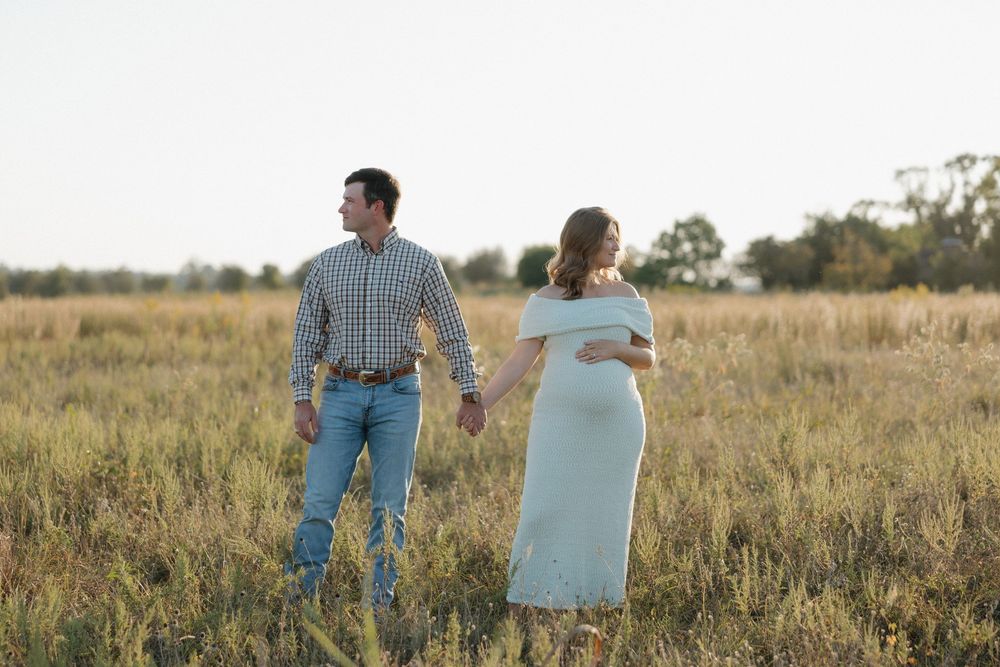 Couple embraces in a golden field at sunset during a romantic maternity photoshoot.