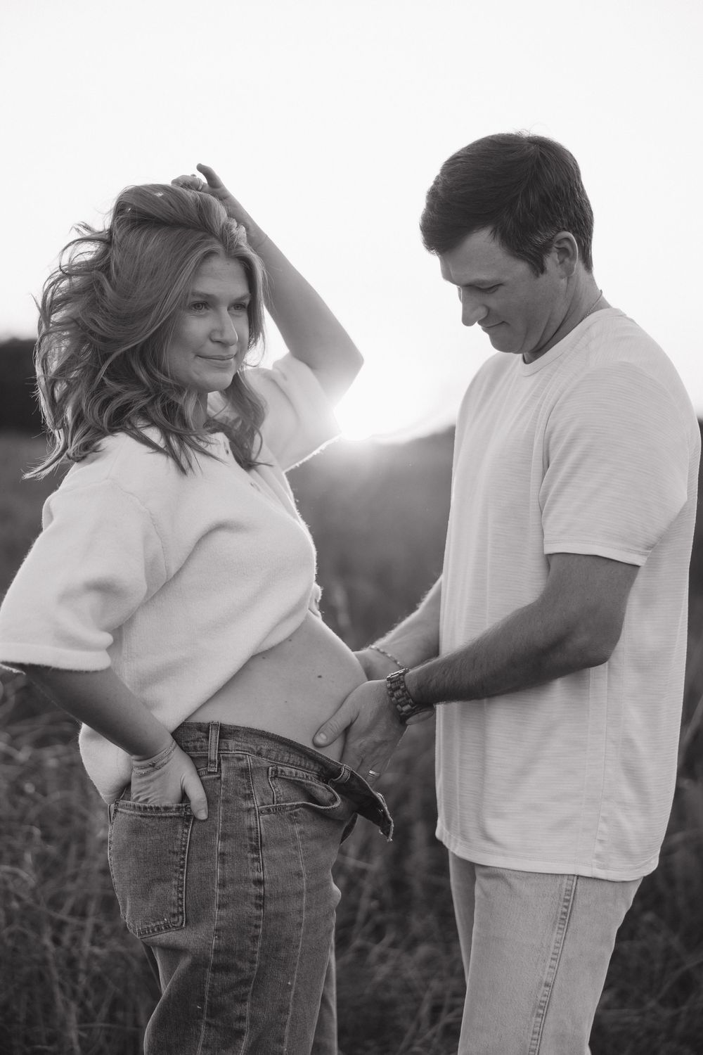 A couple in white shirts and jeans embrace lovingly in a romantic outdoor photoshoot sequence at sunset.