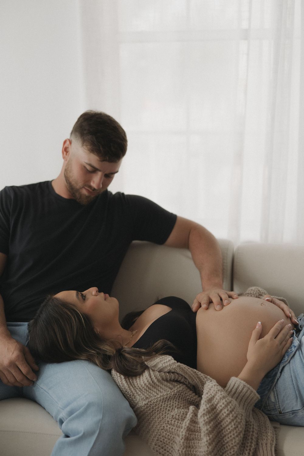 An intimate couple shares a quiet moment on their couch as they anticipate their new arrival together.