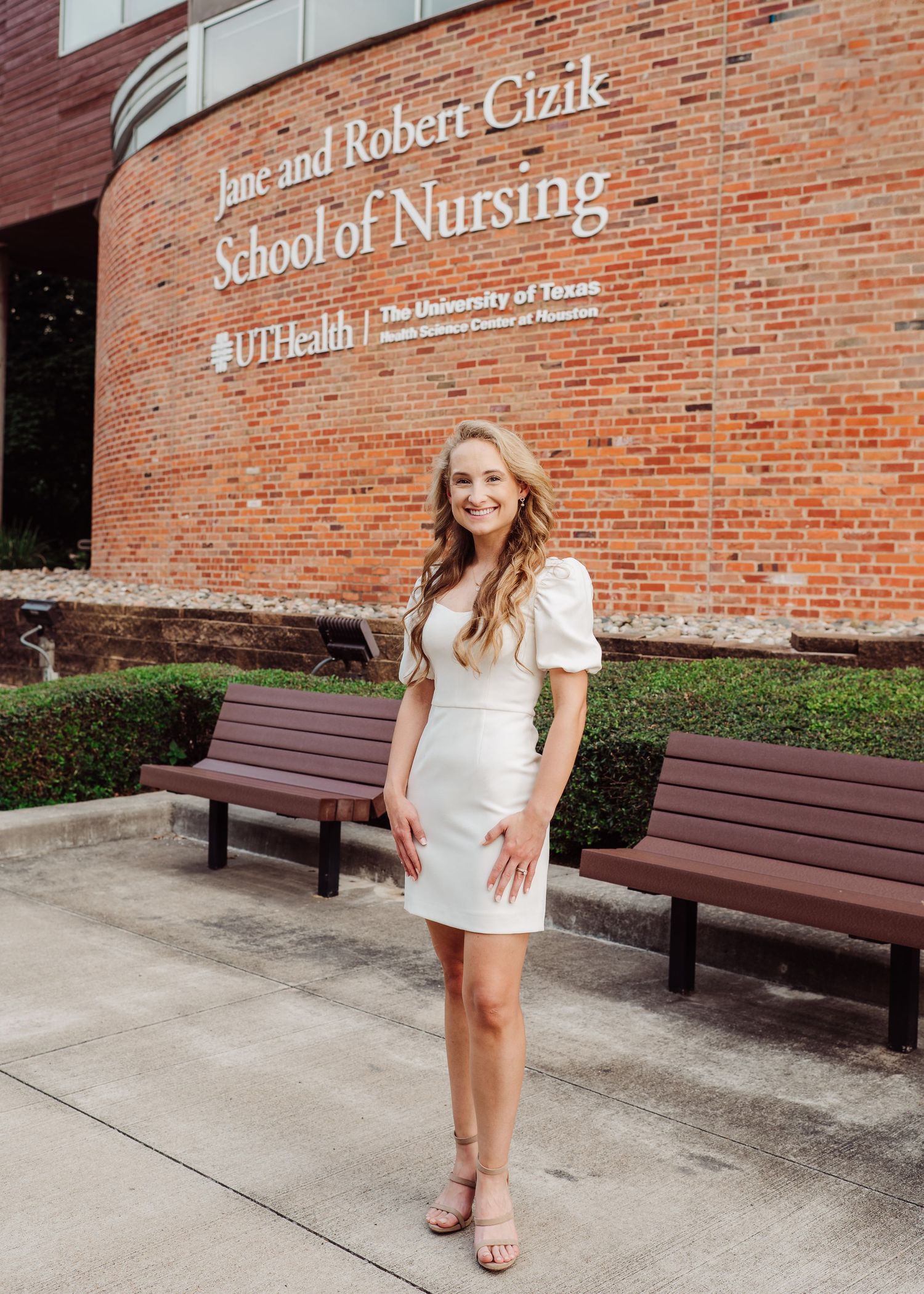 Young woman in white dress poses outside Jane and Robert Cizik School of Nursing at UTHealth Houston.