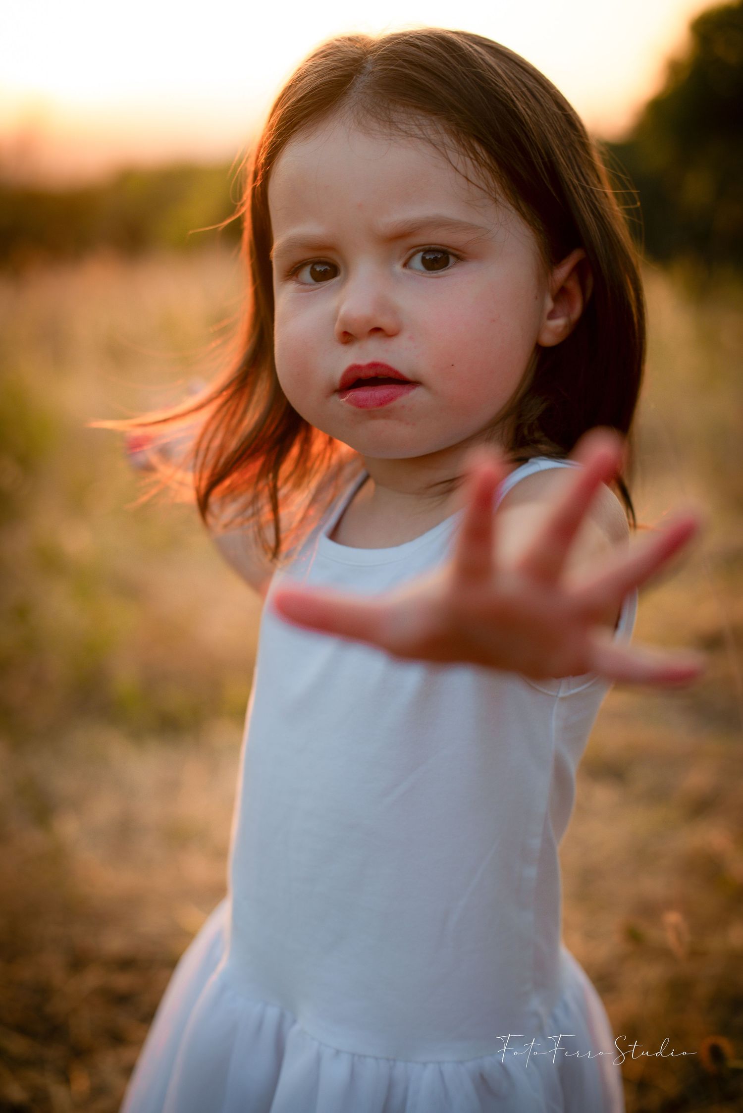 Portrait of young child in white dress at sunset with wind-swept hair.