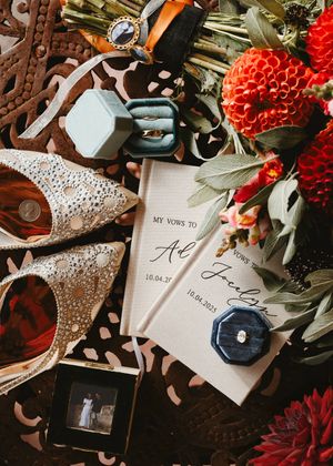 New Mexico Wedding flat lay with vow books, rings, bridal heels, and red dahlia flowers arrangement.