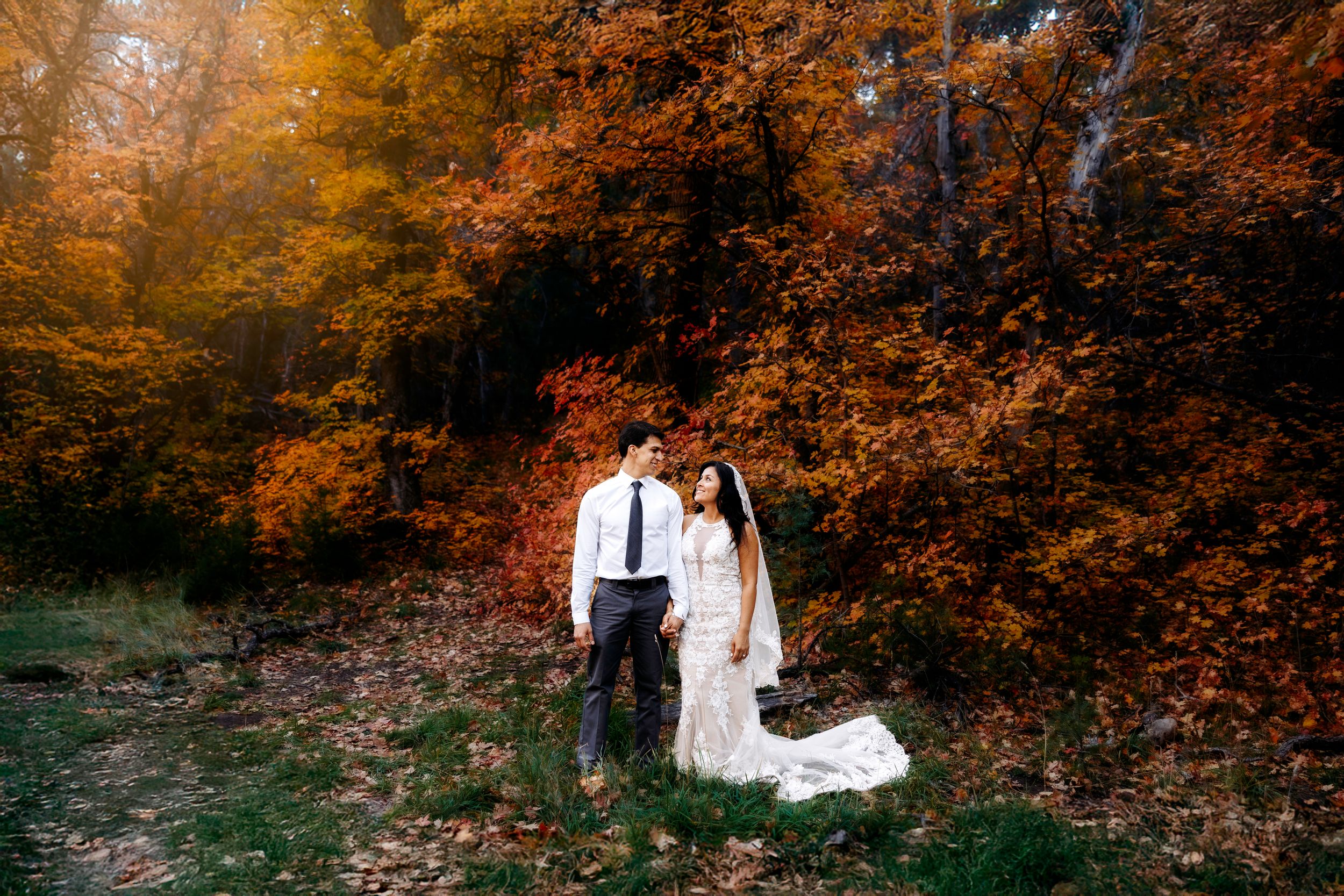 Bride and groom embrace in a stunning Fourth of July Canyon autumn forest with vibrant orange and red foliage during fall wedding.