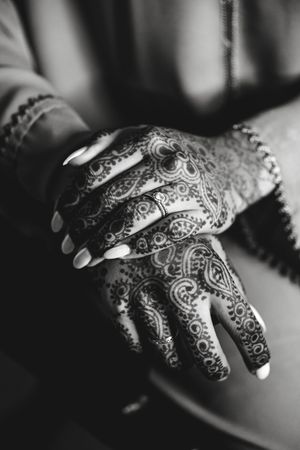 Black and white photo of hands adorned with intricate mehndi henna patterns and rings.