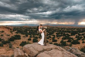 Wedding Couple kissing on desert rock formation under dramatic stormy sunset sky in New Mexico.