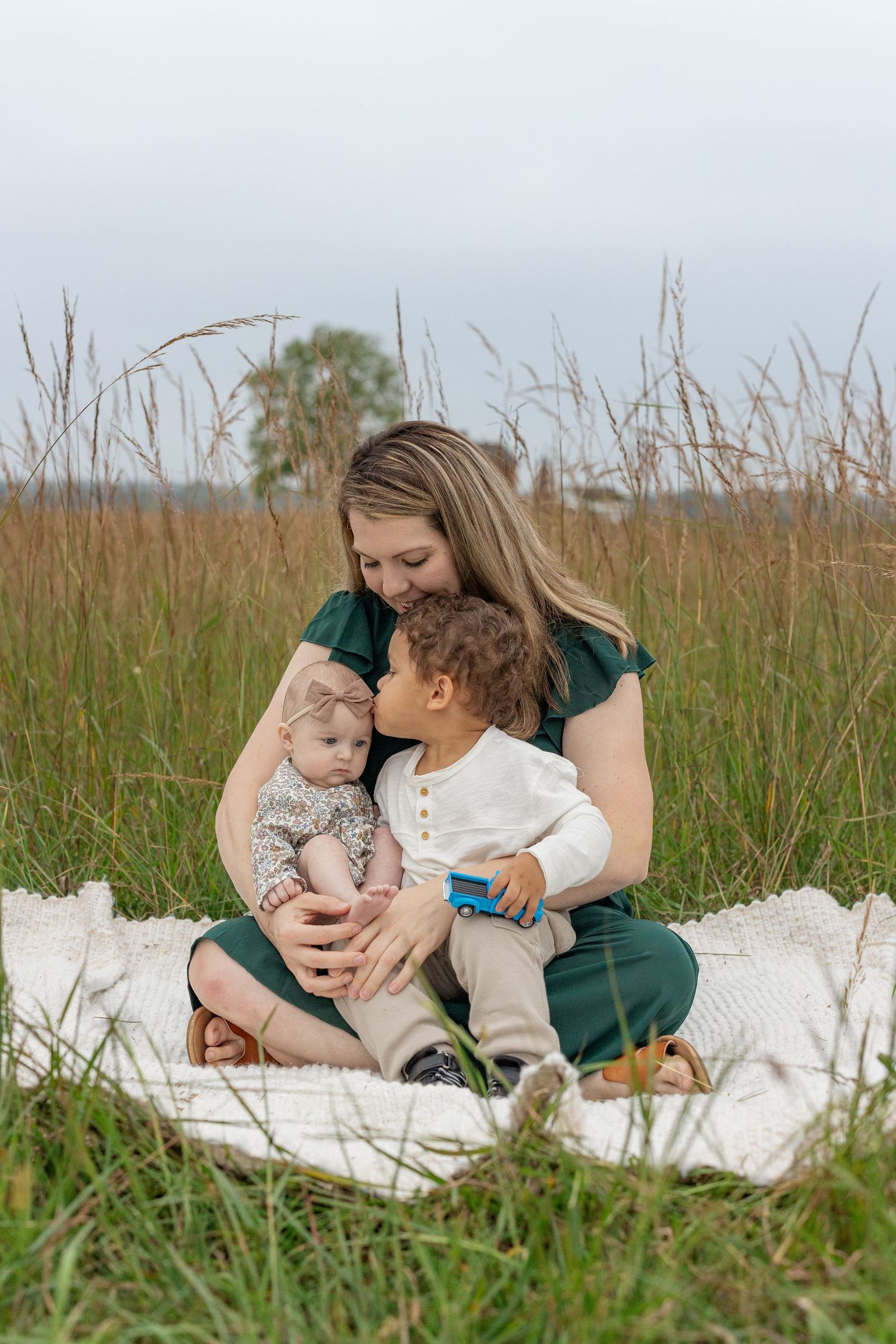 Tender family moment captured on blanket in tall grass field.