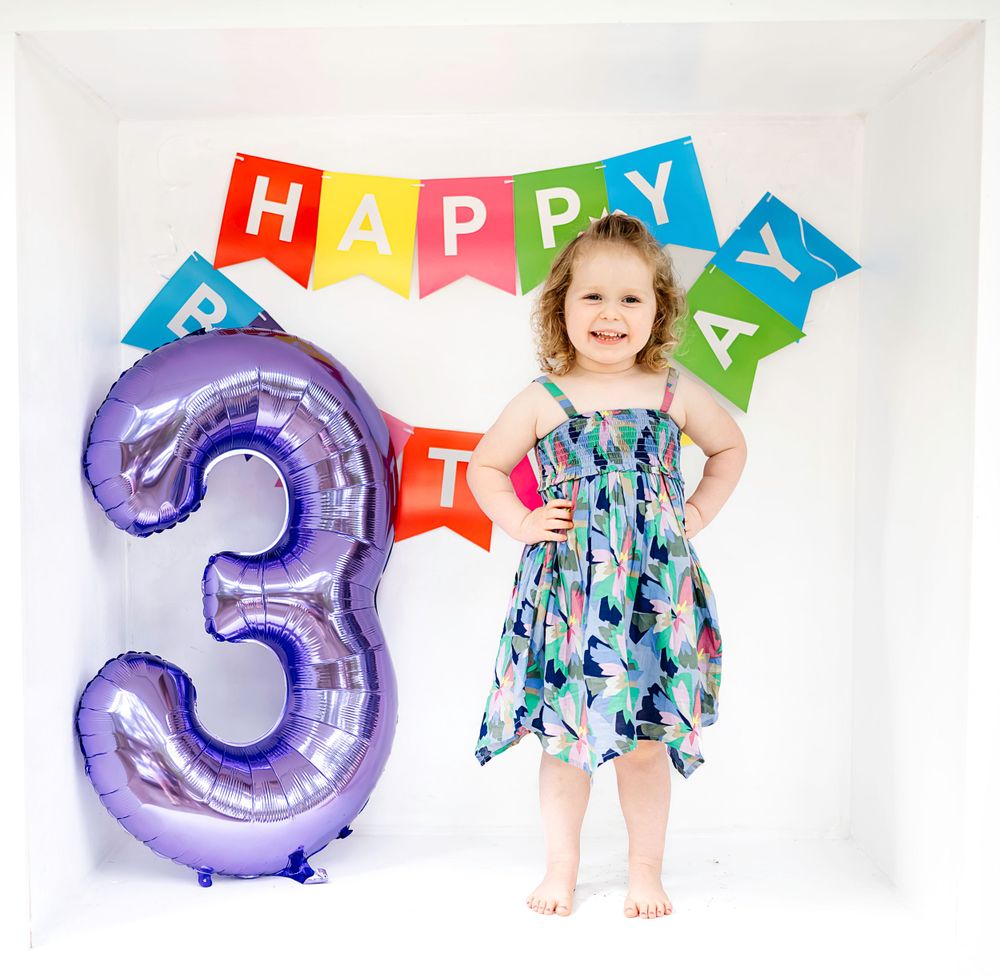 Festive birthday scene with large purple number 3 balloon and colorful Happy Birthday banner against white backdrop.