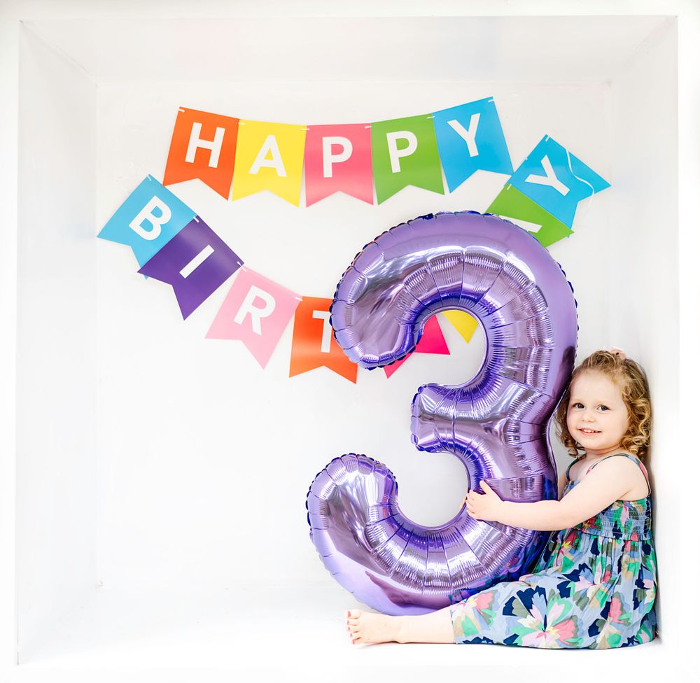 Rainbow birthday banner with purple number 3 balloon against white backdrop.