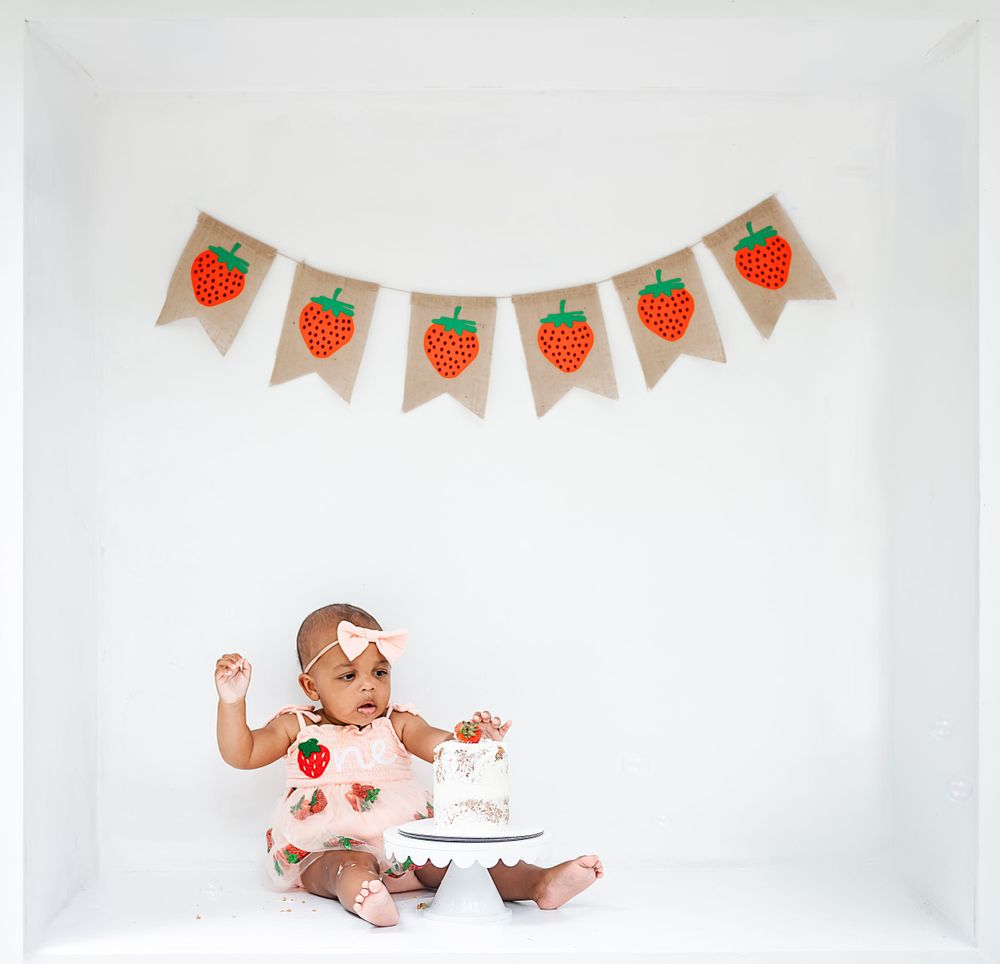 A birthday celebration with strawberry banner decorations and a small cake on white background.
