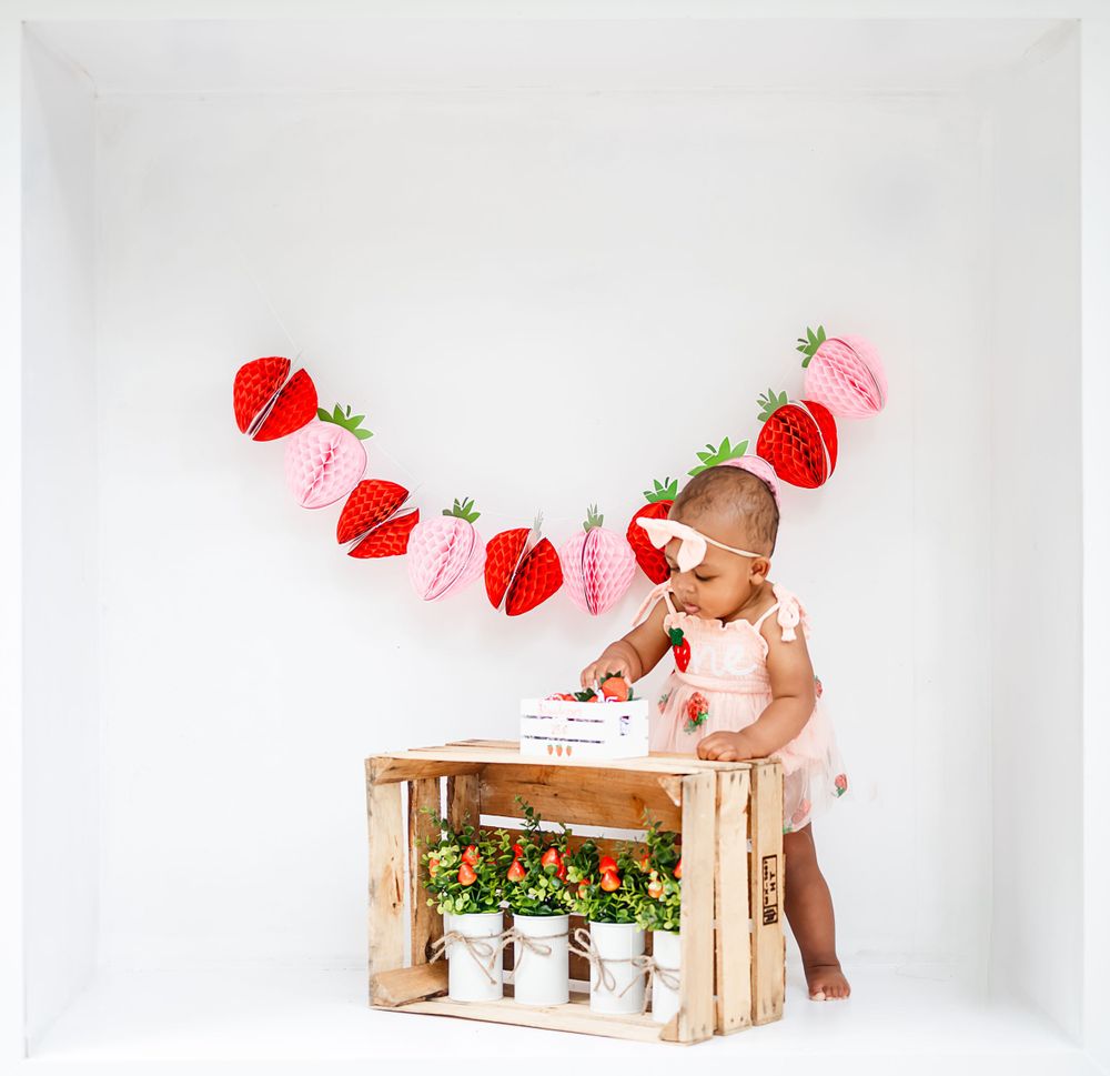 A festive setup with red and pink strawberry garland decorations and a wooden crate.