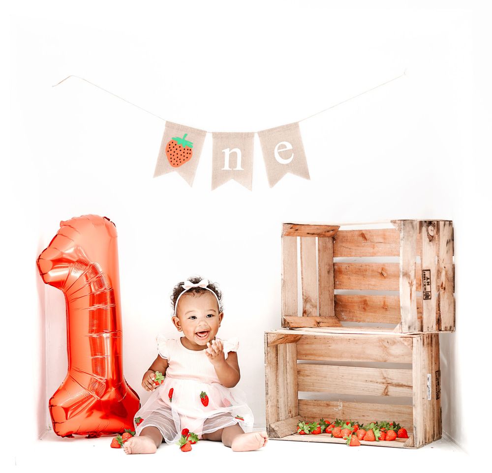First birthday setup with coral balloon number 1, wooden crates and strawberry banner decorations.