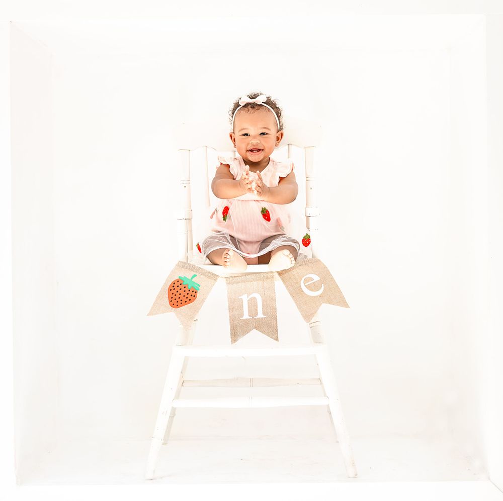 White high chair decorated with strawberry themed banner for first birthday celebration.