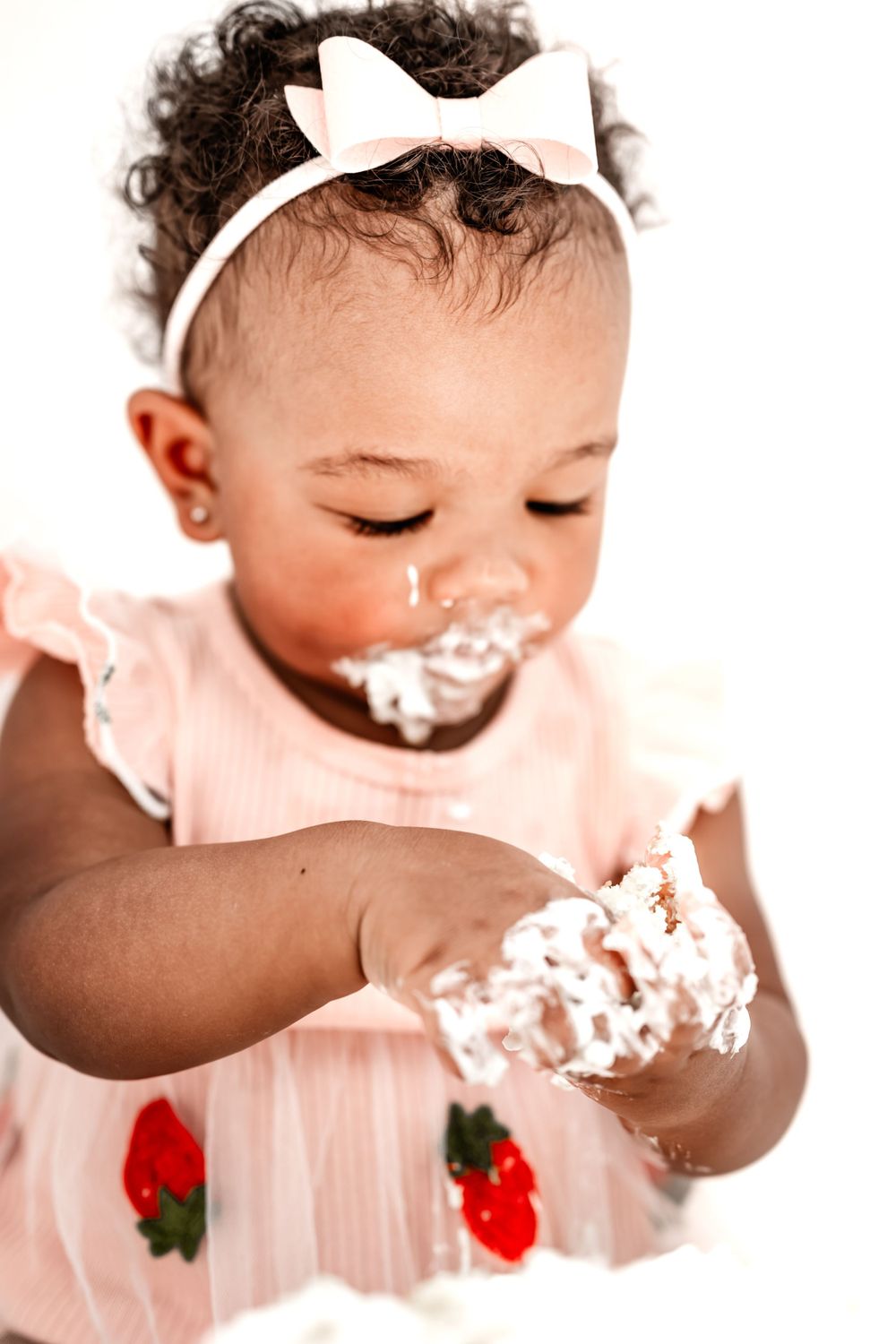 Close up of a cake smash moment with white frosting and pink dress with strawberry details.