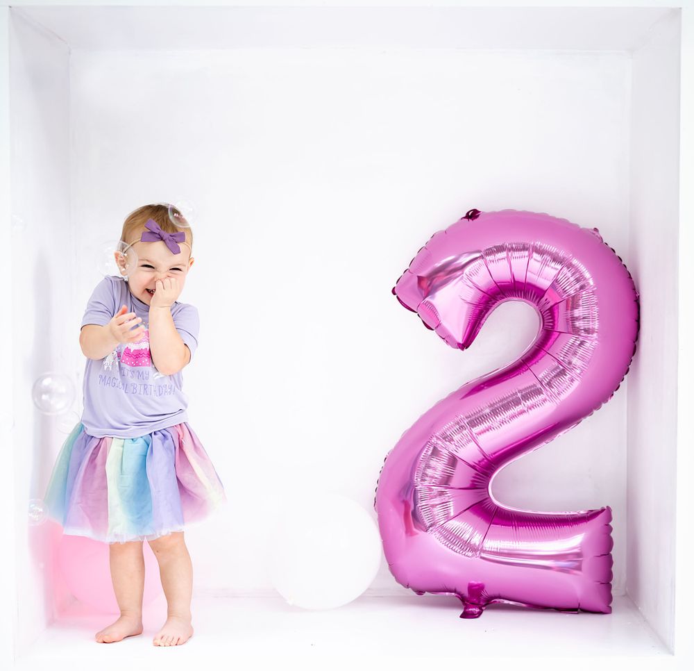 A pastel-colored birthday scene featuring a large pink number 2 balloon against white background.