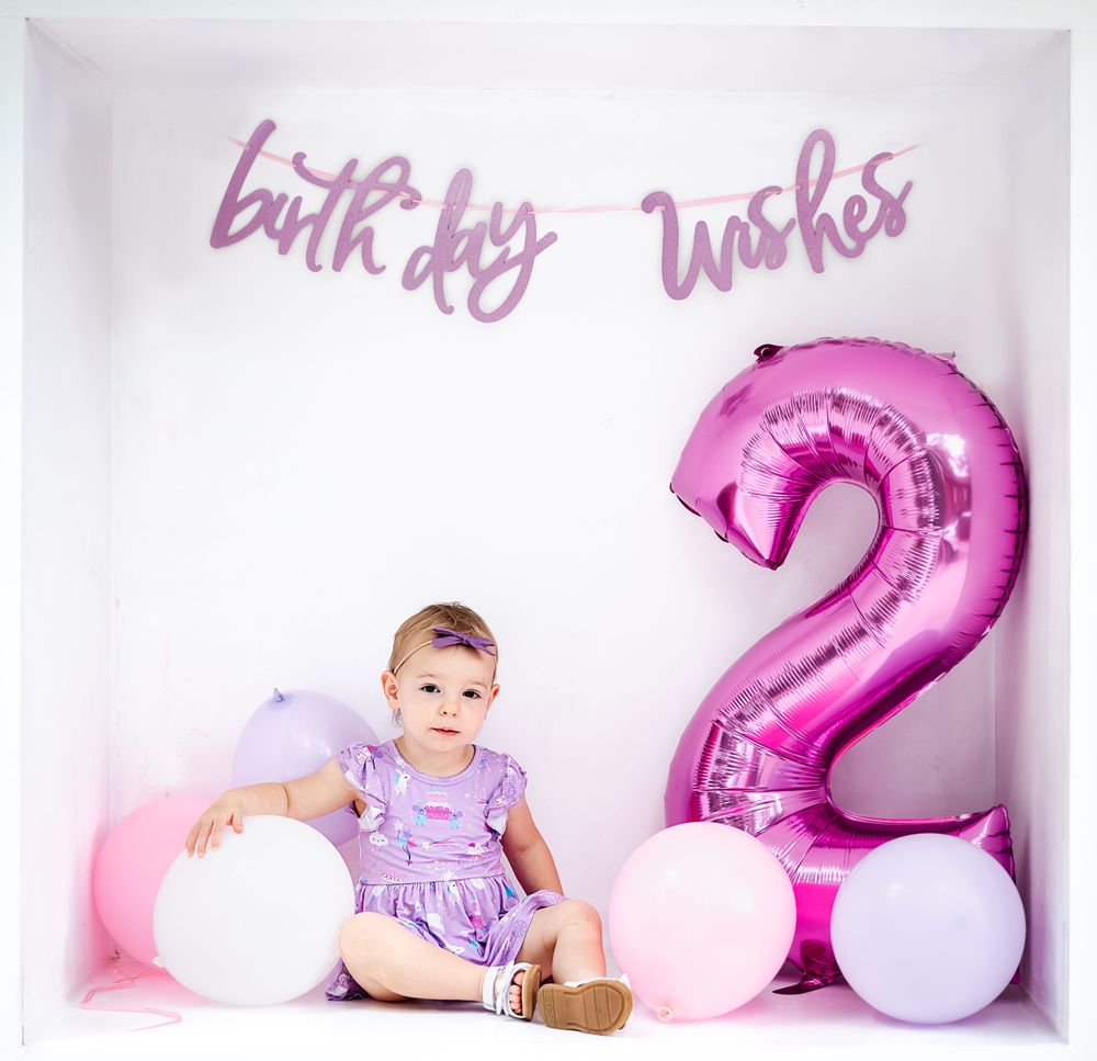 Birthday photoshoot setup with pink number 2 balloon and white balloons against a light pink background.