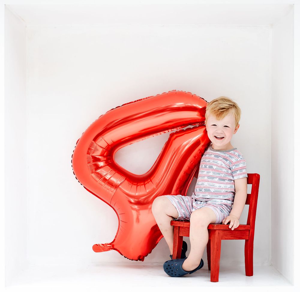 Red number 4 balloon and small red chair against white background for birthday photos.